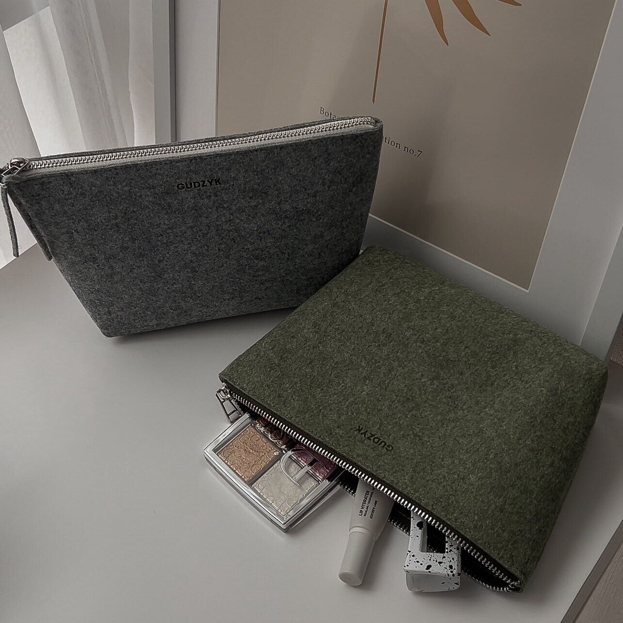Green and grey felt cosmetic bags with makeup items on a light surface