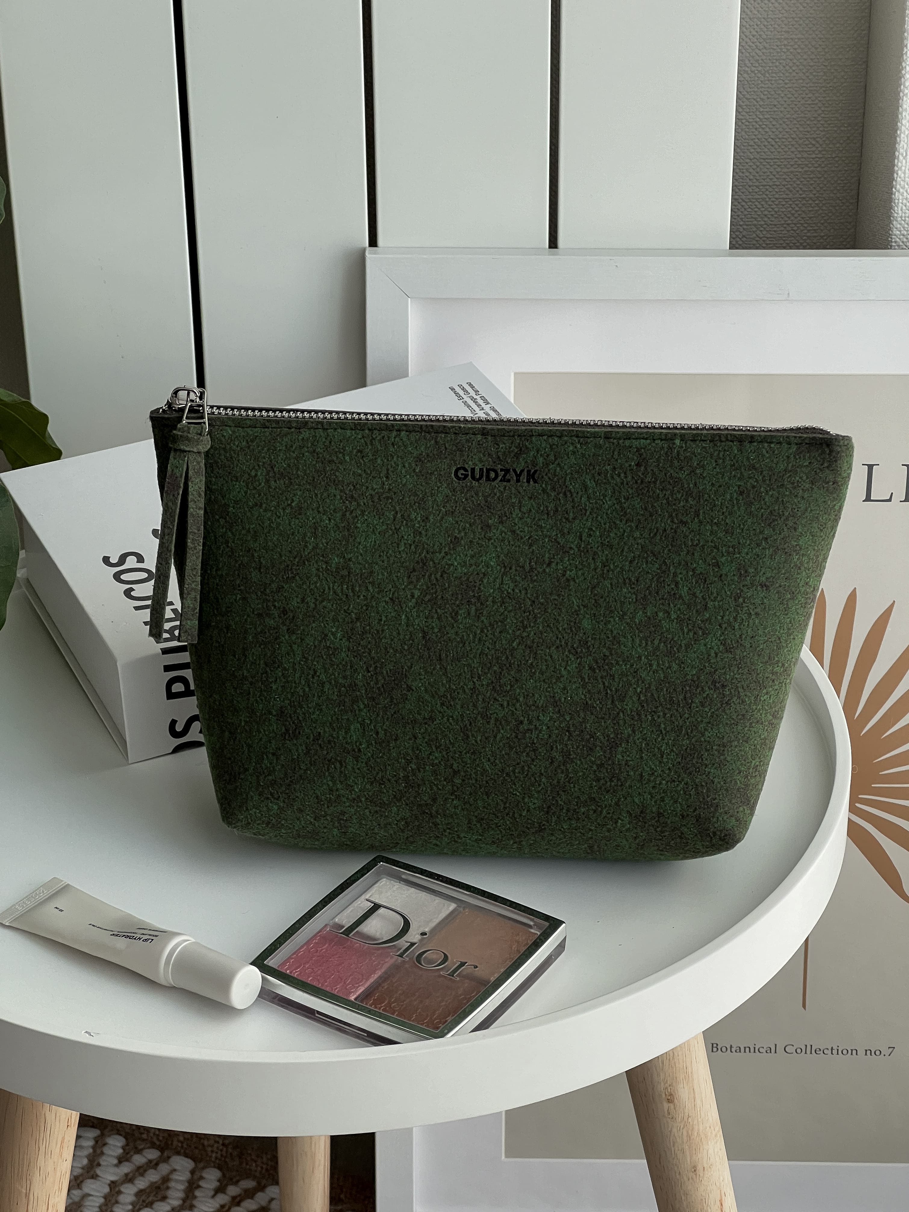 Green clutch bag on a white table with cosmetic items