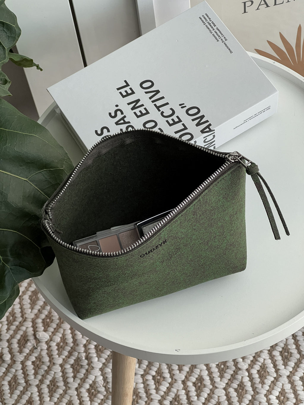 Green pouch on a white surface with a book in the background