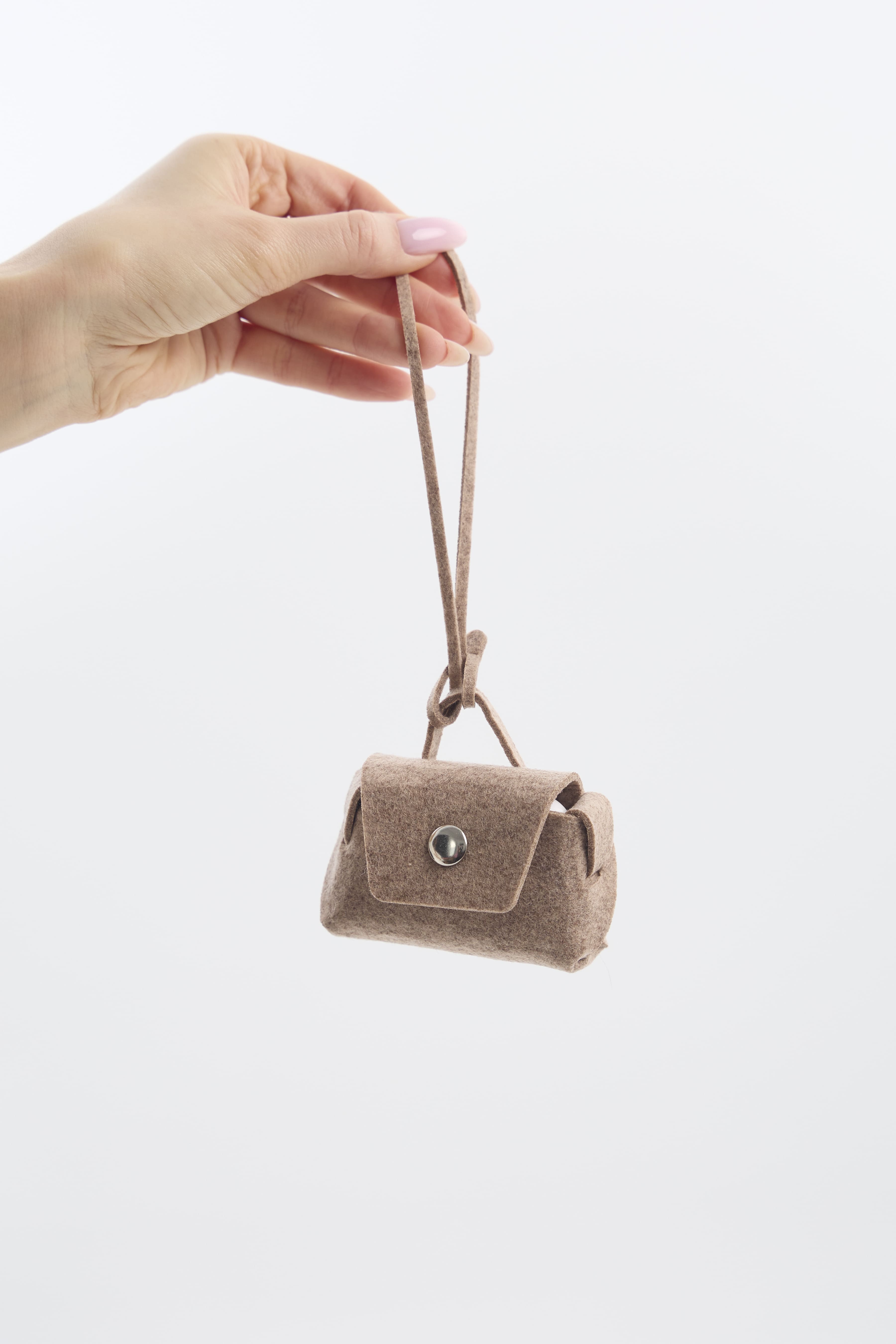 Hand holding a small beige felt pouch against a white background