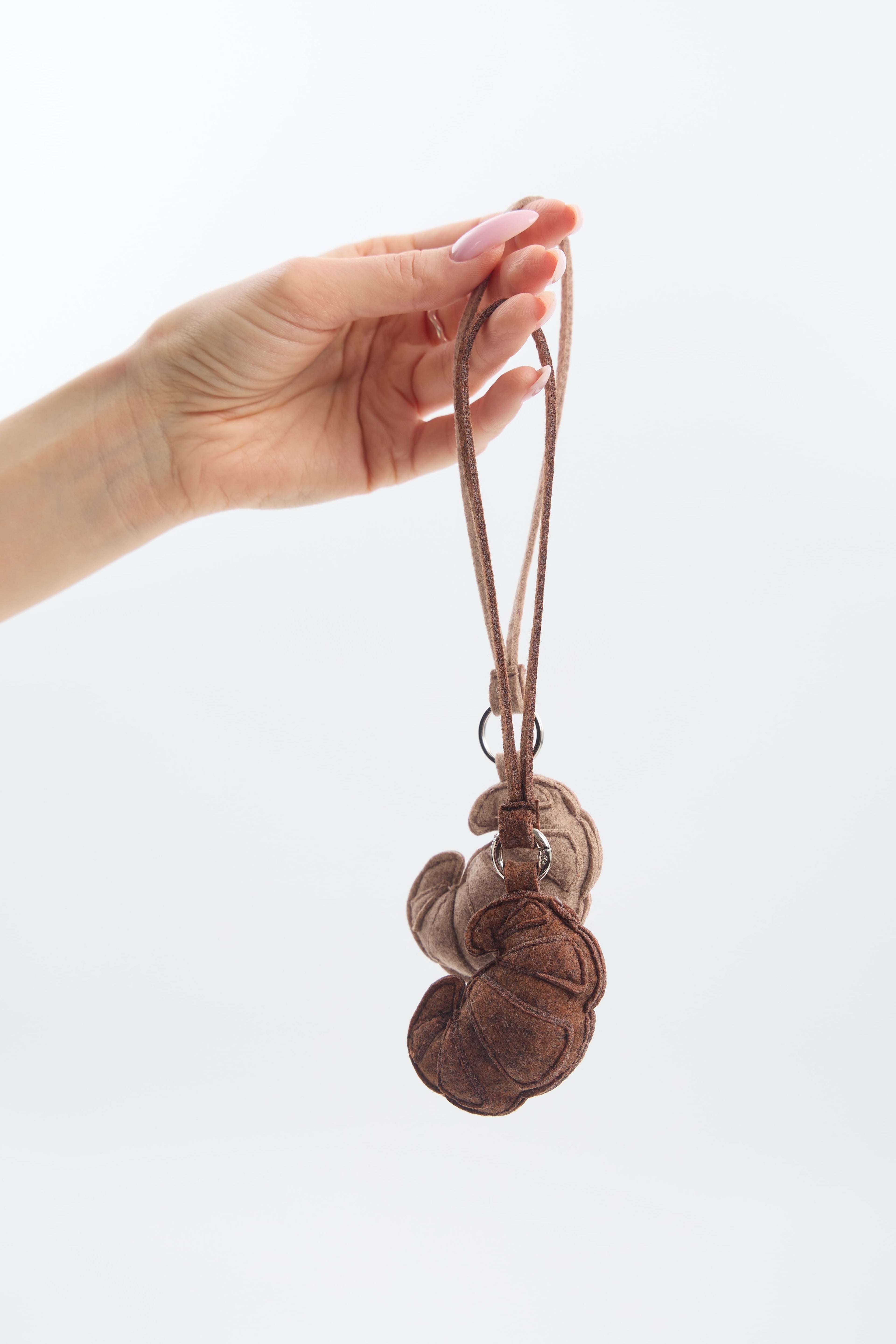 Hand holding a small brown eco felt keychain with a strap against a white background