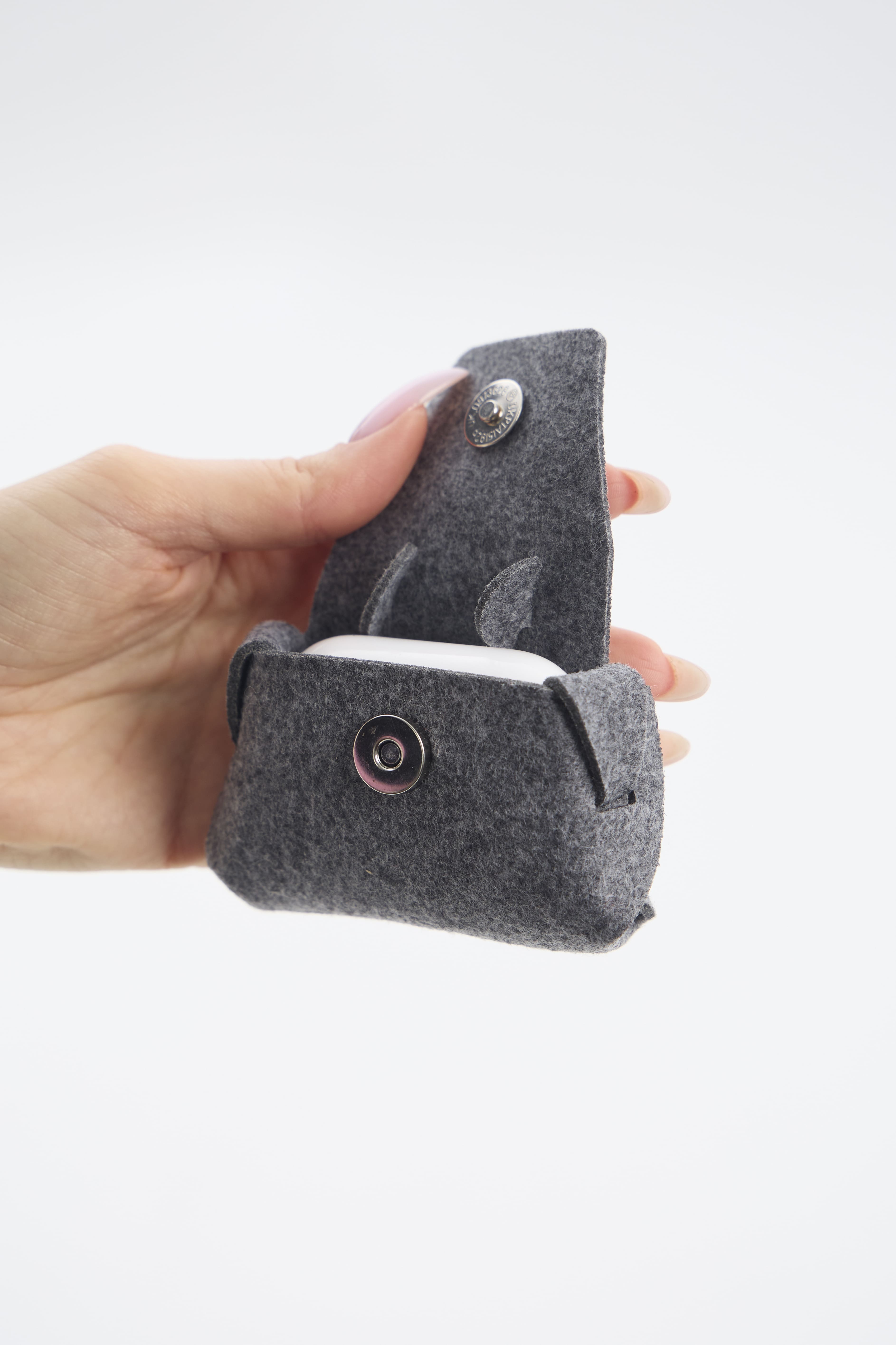 Hand holding a gray felt pouch with a button on a white background