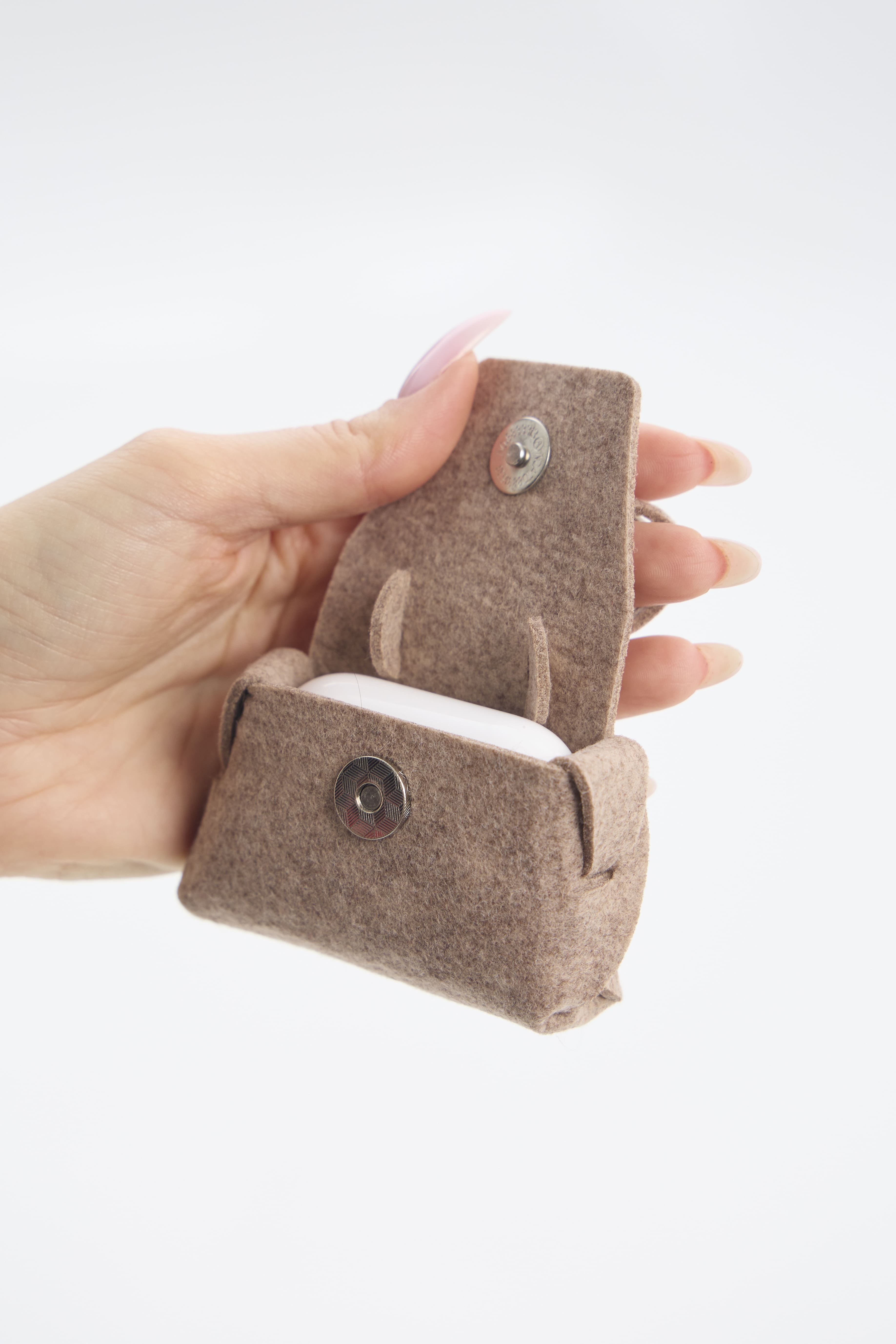Hand holding a small beige felt pouch with button on a white background