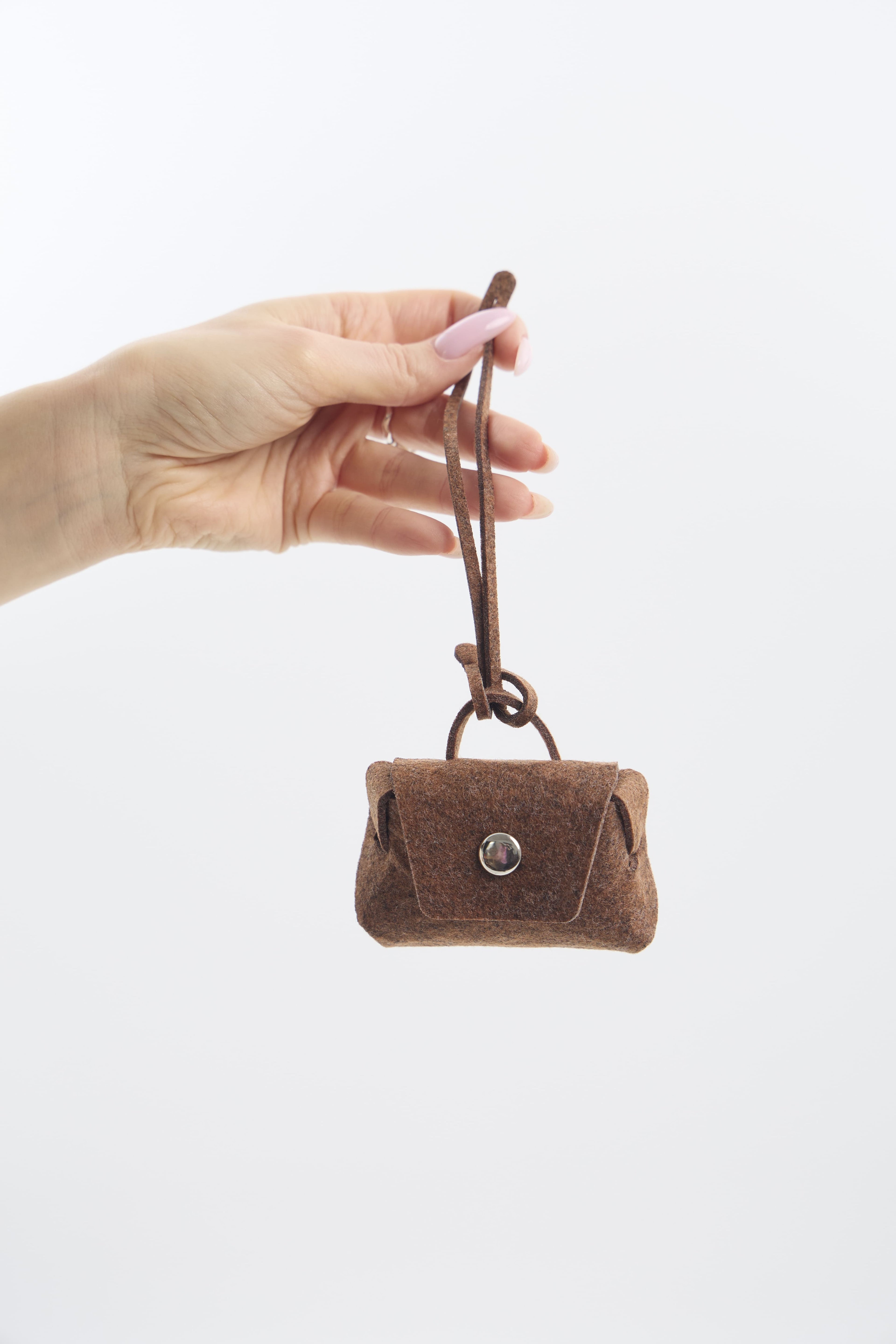 Hand holding a small brown felt purse against a white background
