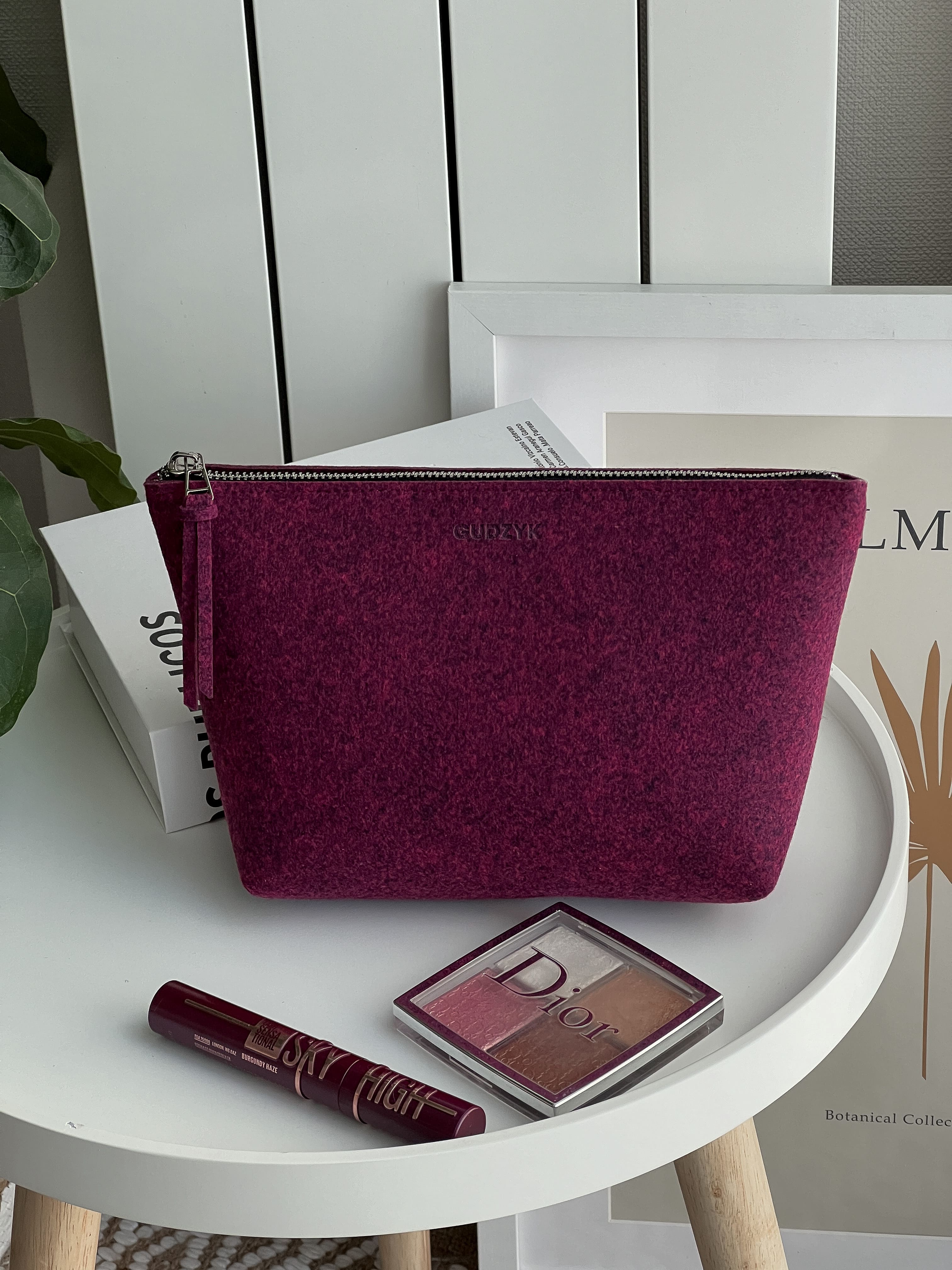 Burgundy make up pouch on a white table with Dior makeup products