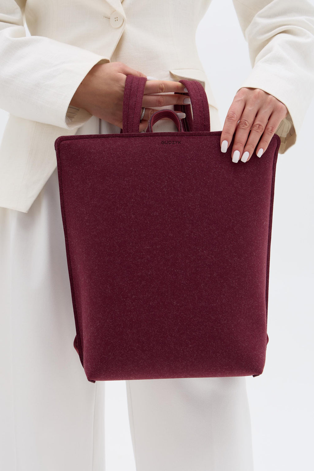 Burgundy backpack held by a person wearing a white outfit