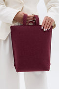 Burgundy backpack held by a person wearing a white outfit