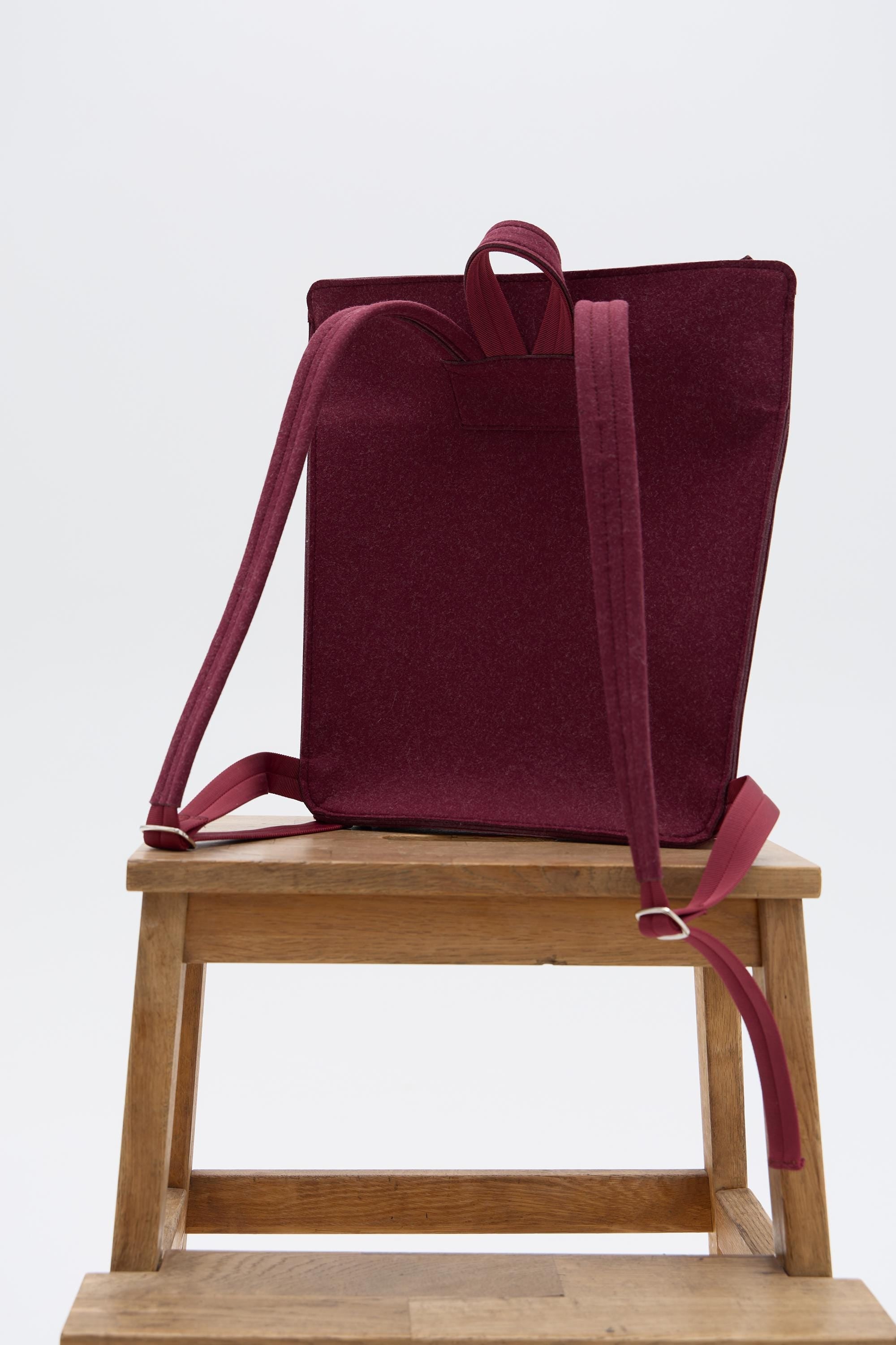 Burgundy backpack on a wooden stool against a white background