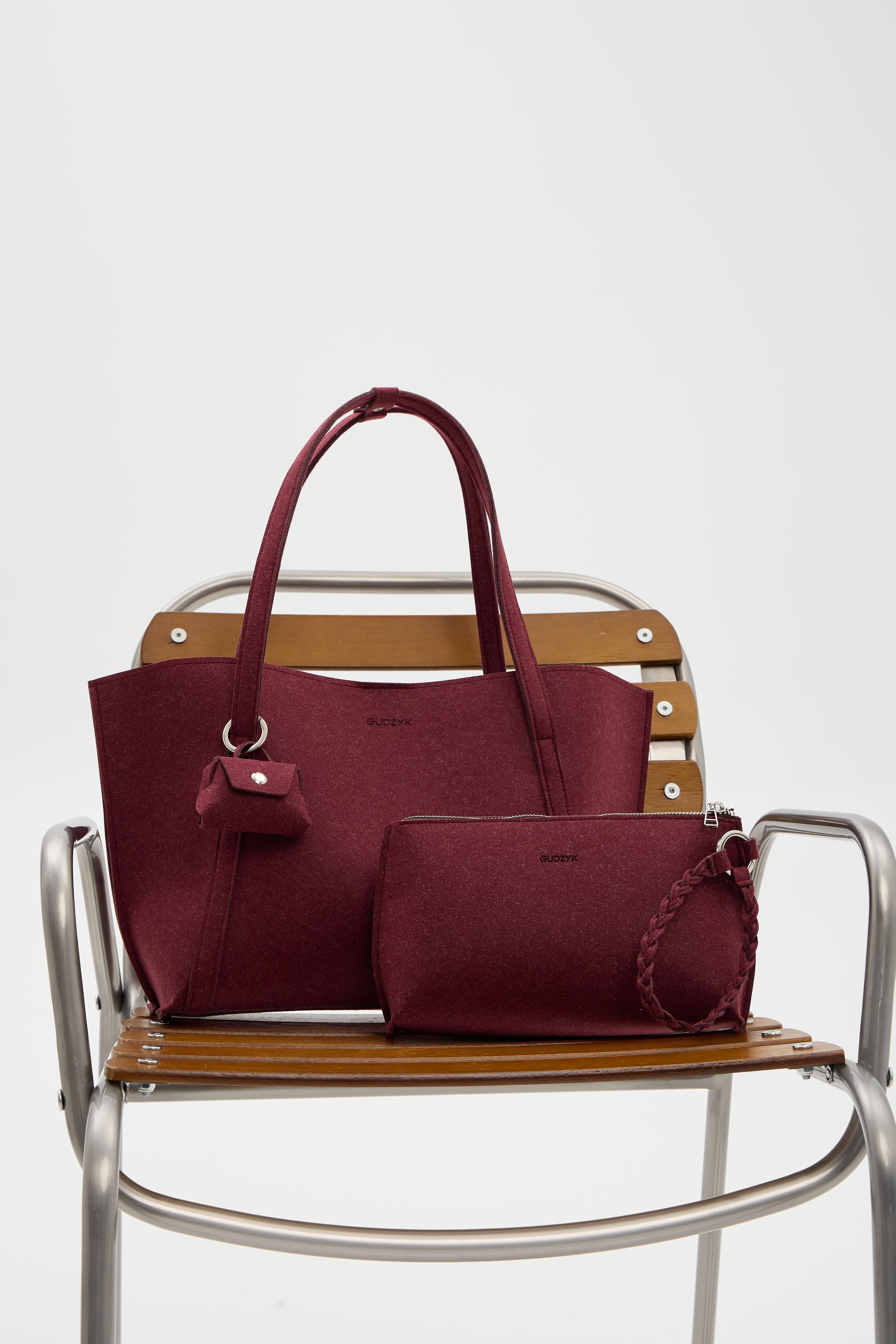 Maroon handbag and matching pouch on a wooden chair with a white background