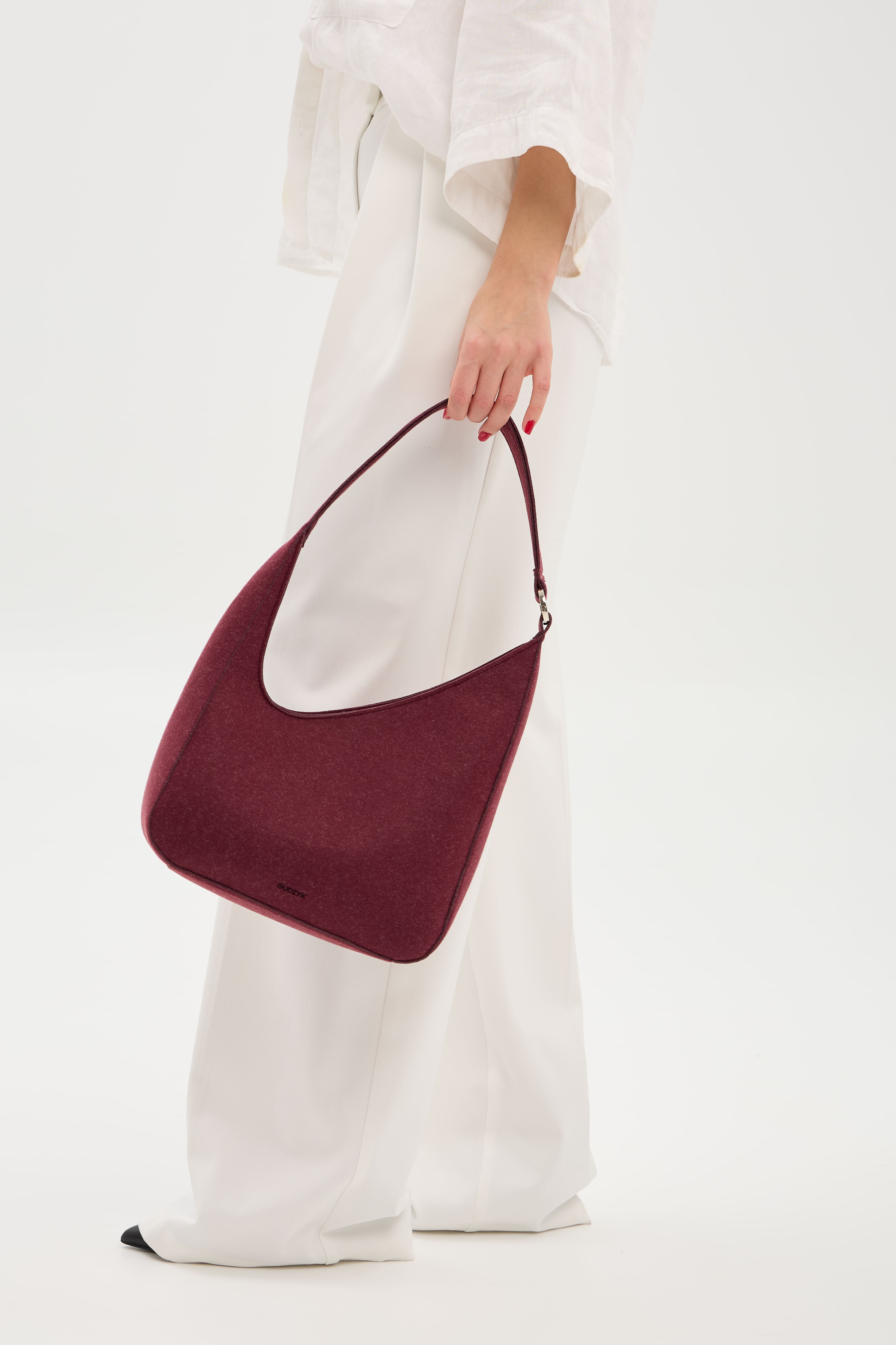 Burgundy handbag held by a person wearing a white outfit on a light background