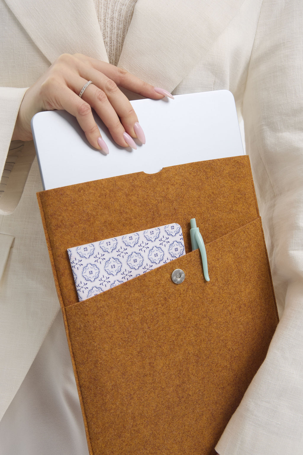 Orange felt laptop sleeve with a white notebook, pen, and patterned workbook.