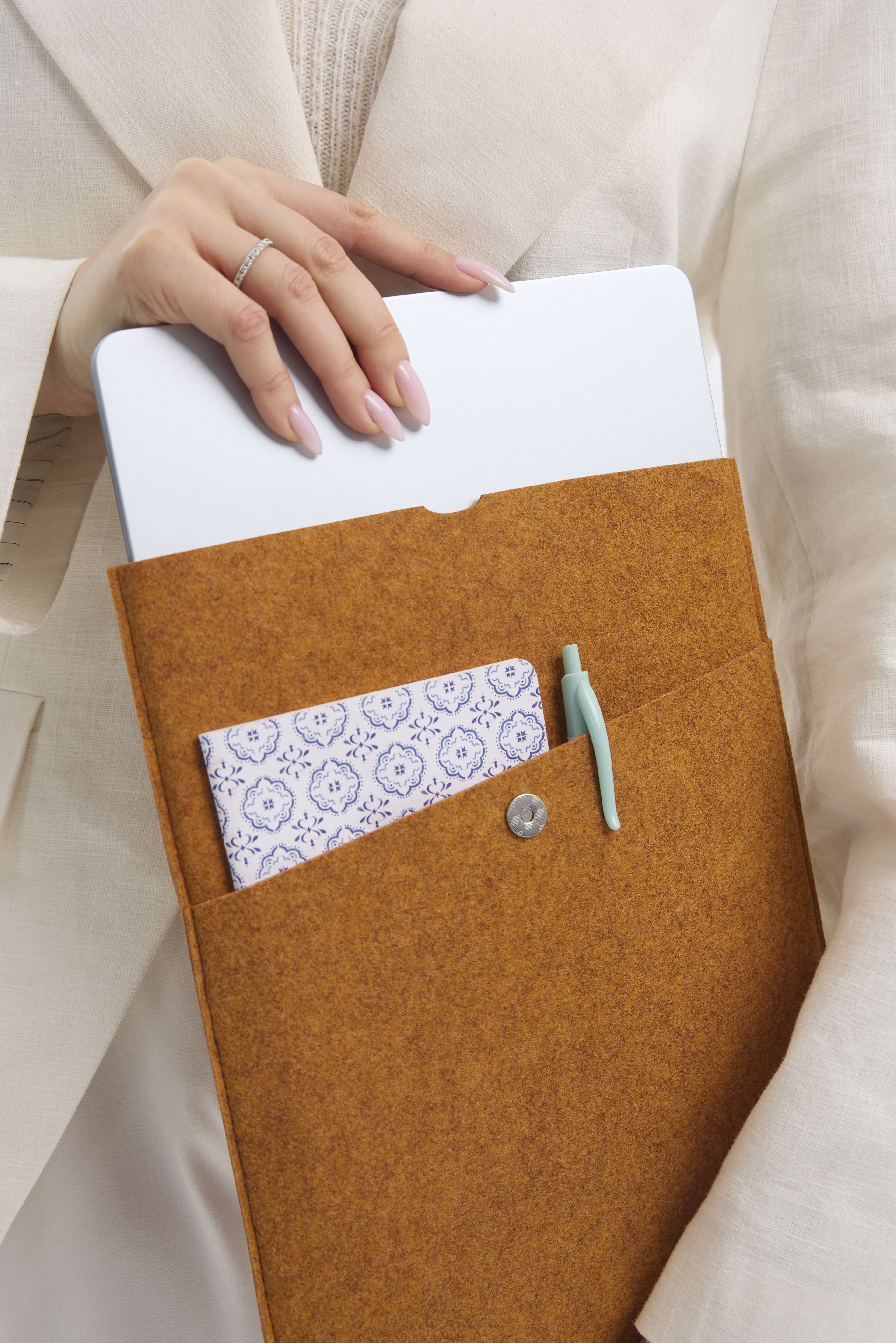 Orange felt laptop sleeve with a white notebook, pen, and patterned workbook.