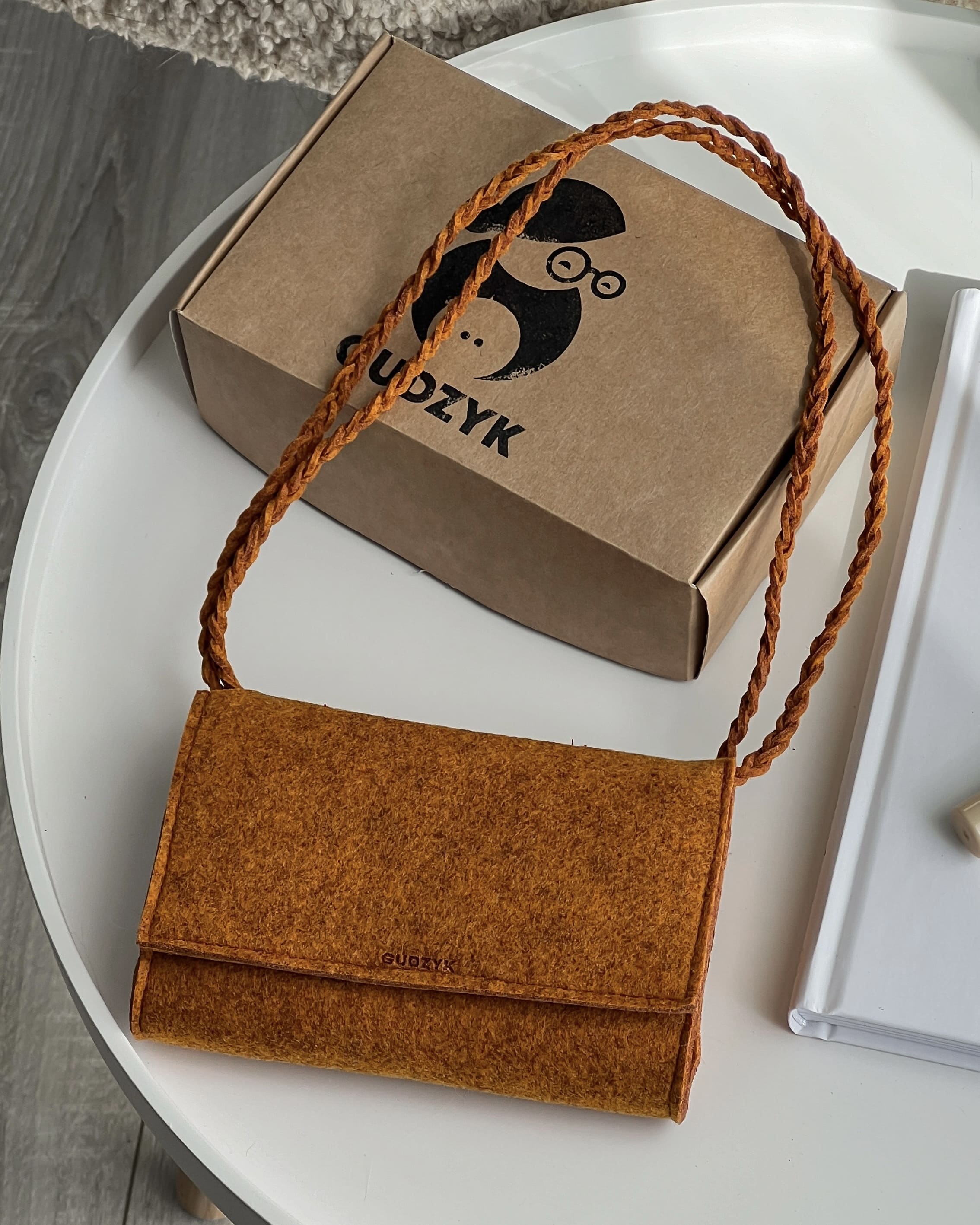 Orange handbag with braided handle on a white surface next to a brown box with 'GUDZYK' branding.