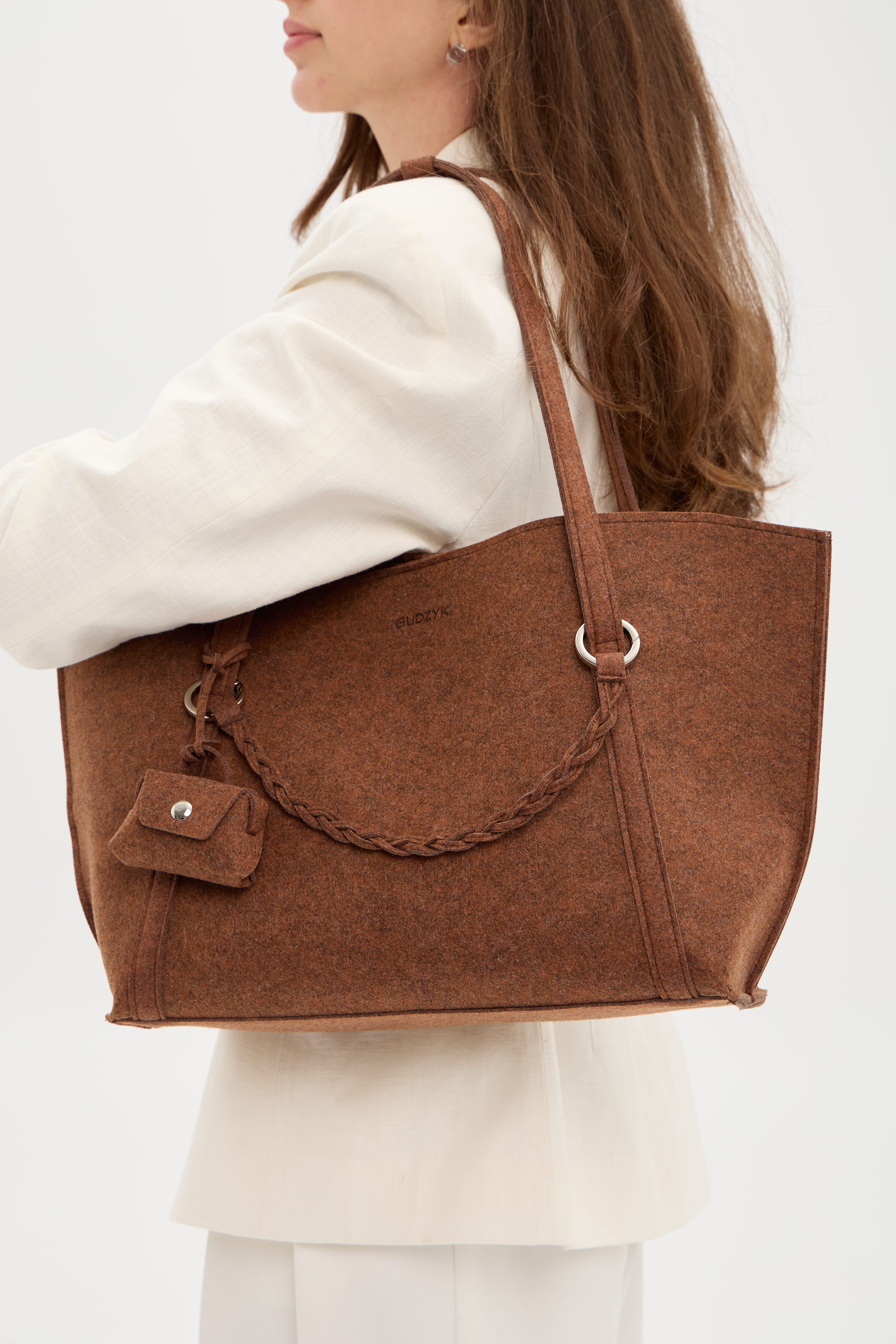 Person carrying a brown tote bag on a plain background