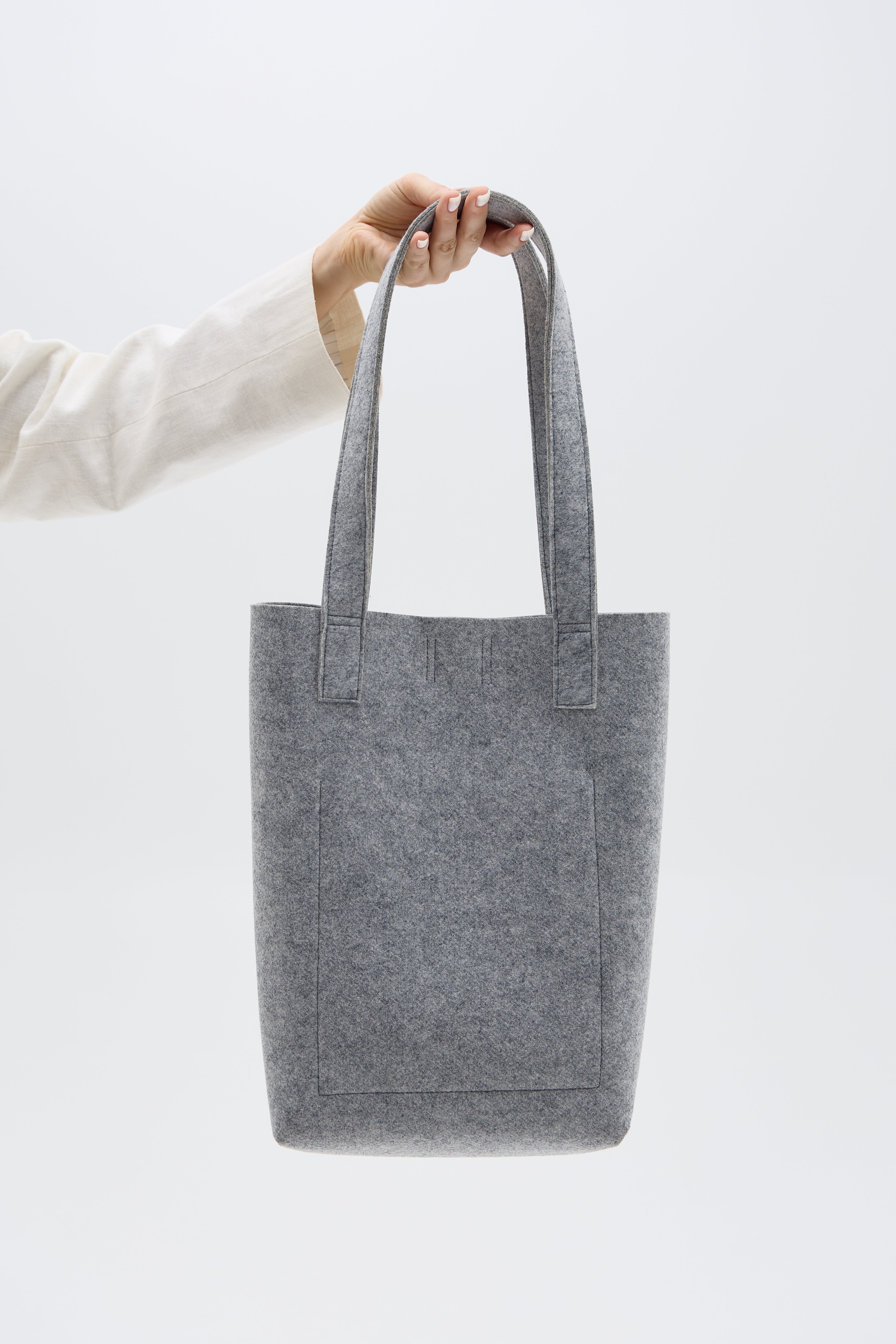 Gray tote bag held by a person against a white background
