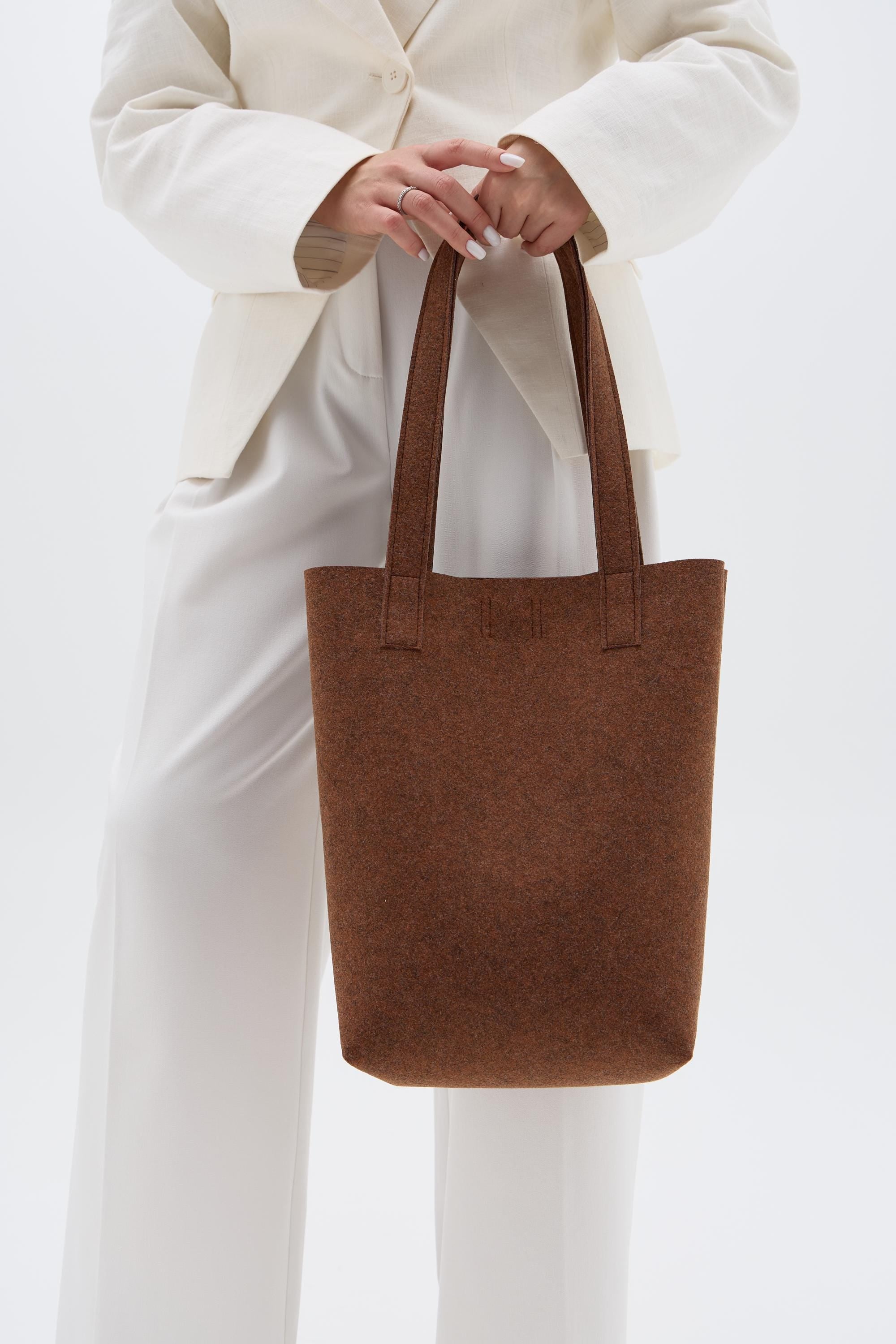 Person holding a brown tote bag against a white background