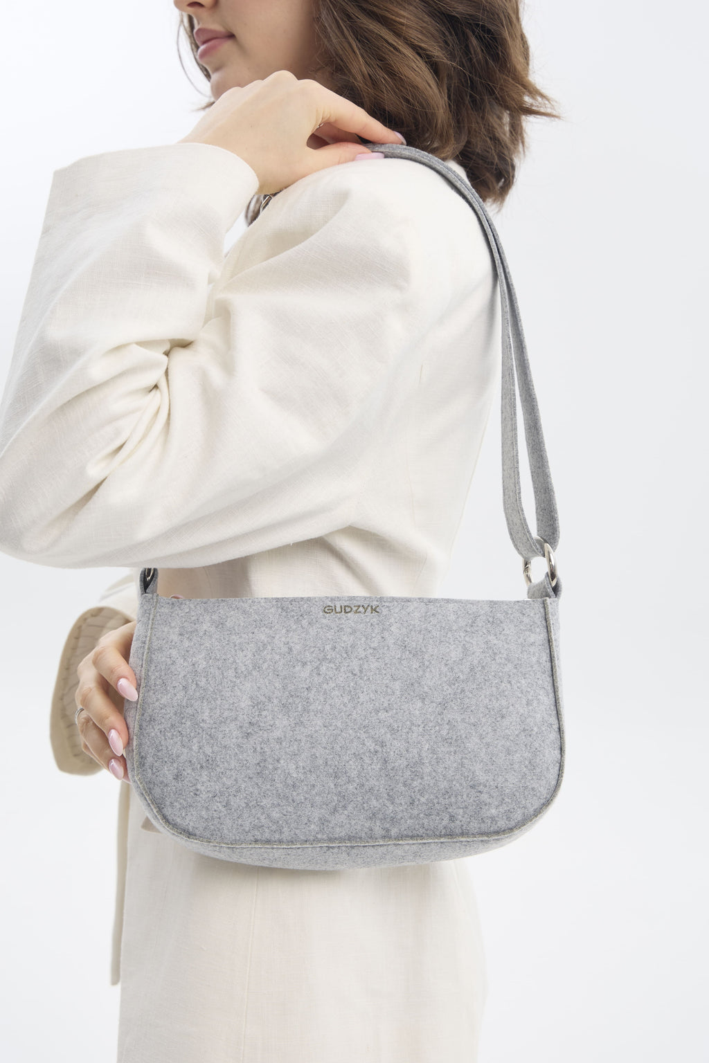 Person holding a gray shoulder bag against a white background