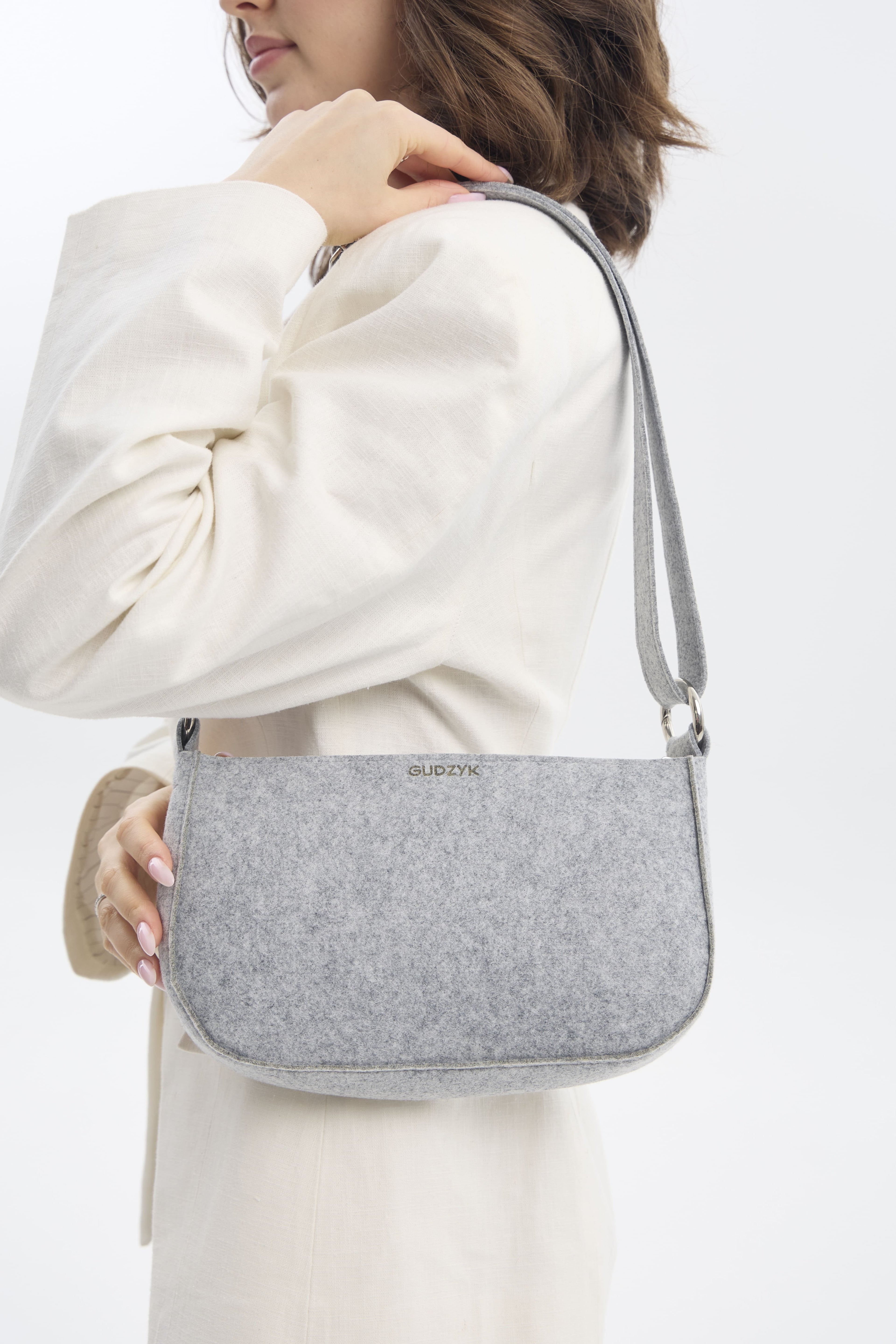 Person holding a gray shoulder bag against a white background
