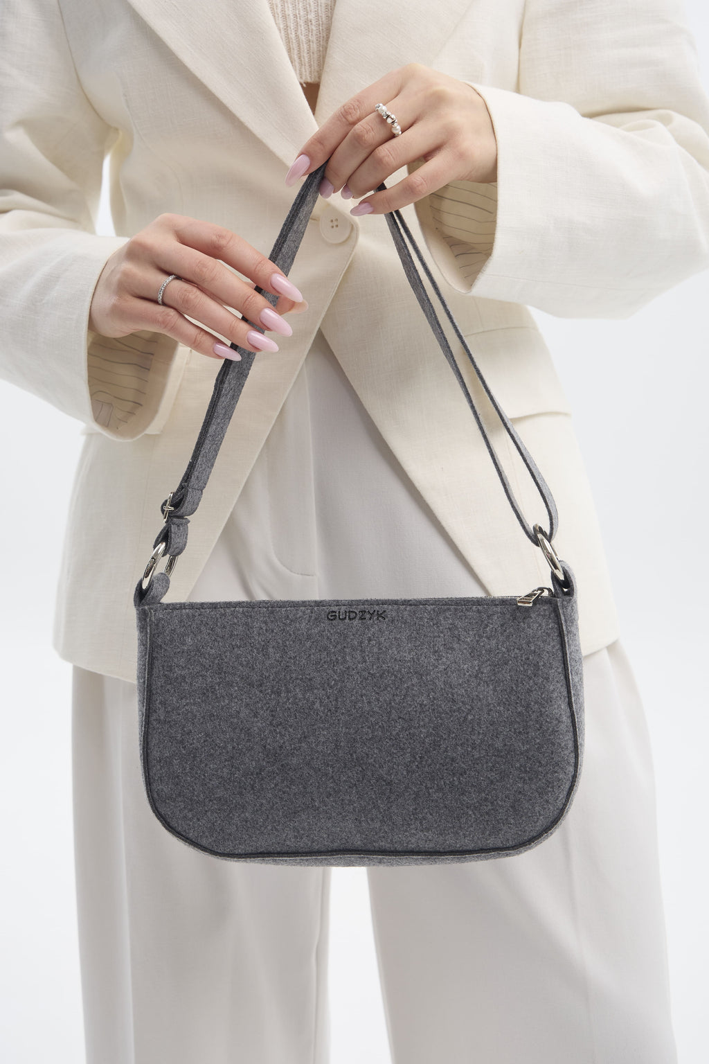 Person holding a gray shoulder bag with a plain background