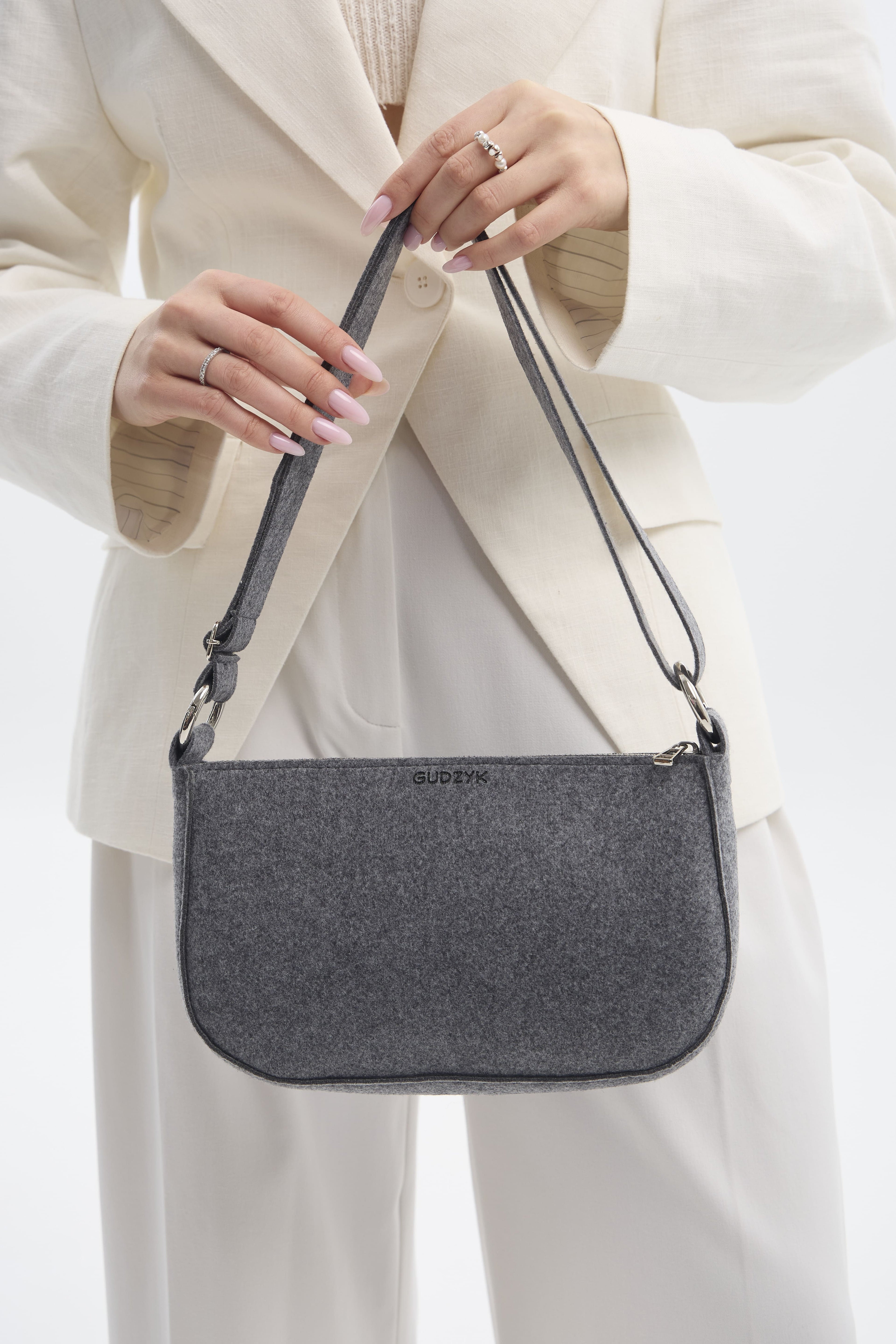 Person holding a gray shoulder bag with a plain background