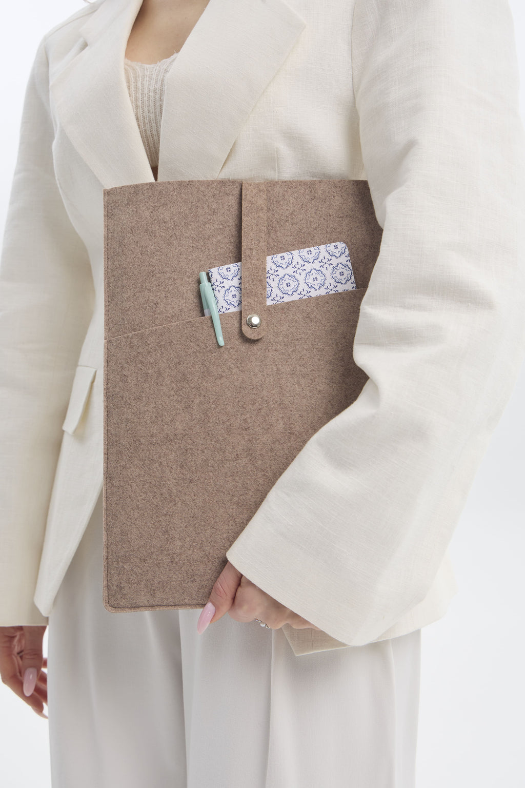 Person holding a beige ecofelt sleeve with a white lace detail on a plain background