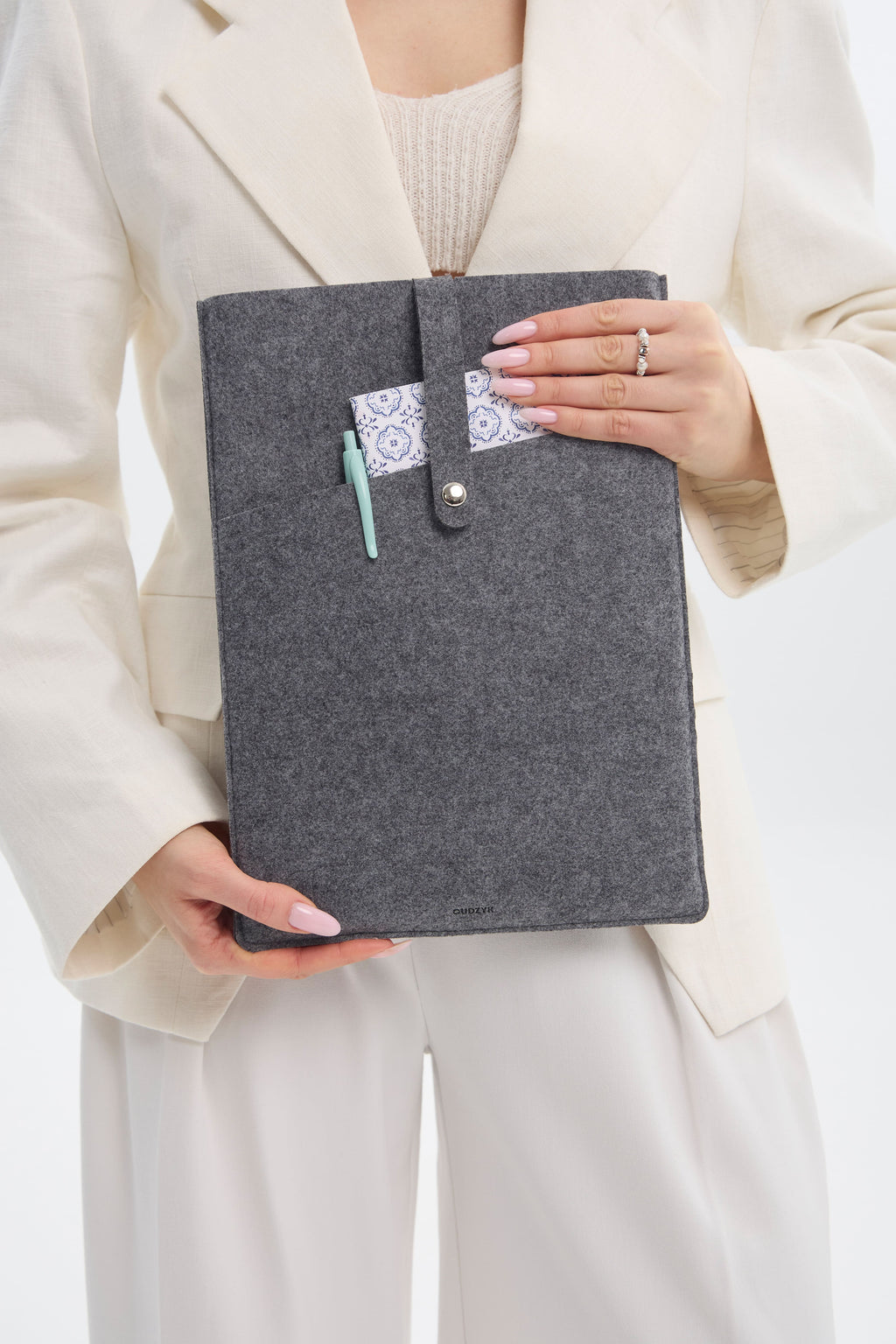 Person holding a gray ecofelt case with a pen and small pouch, wearing a beige outfit.
