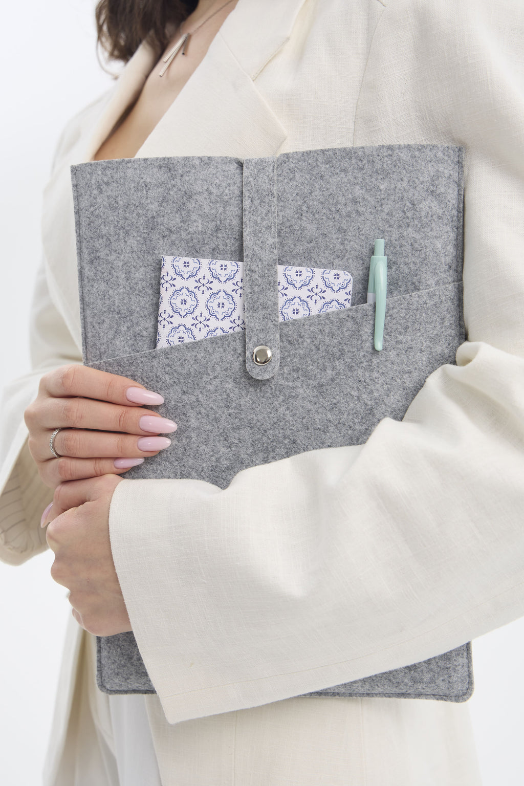 Person holding a gray felt pouch with decorative pocket and pen, wearing a white coat.