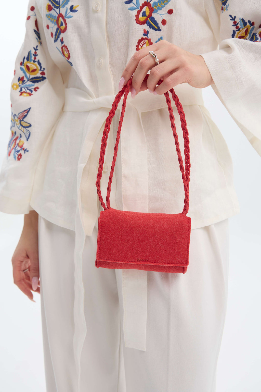 Person holding a red handbag with a white outfit featuring colorful embroidery.