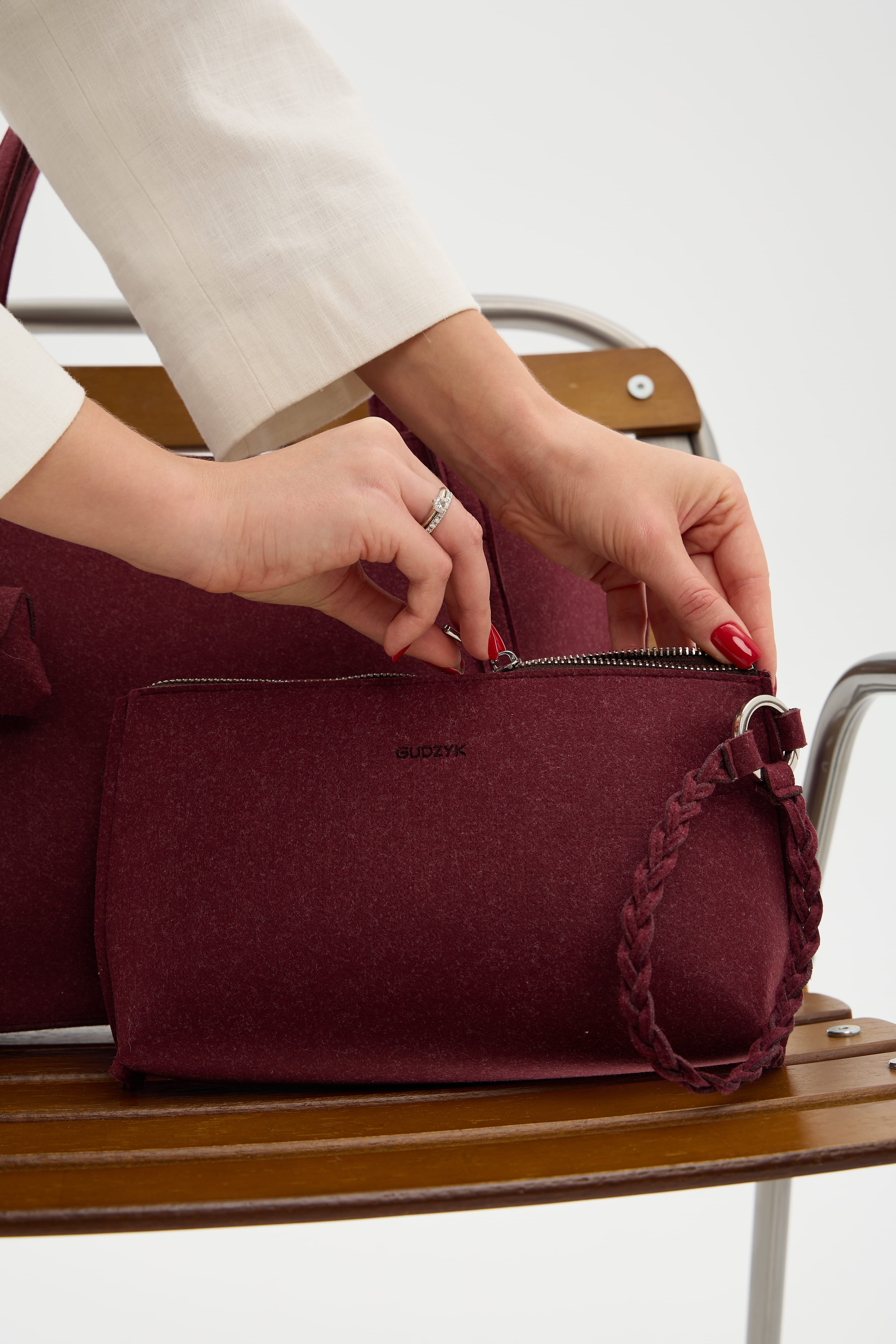 Person opening a burgundy handbag with a visible brand logo on a wooden chair.