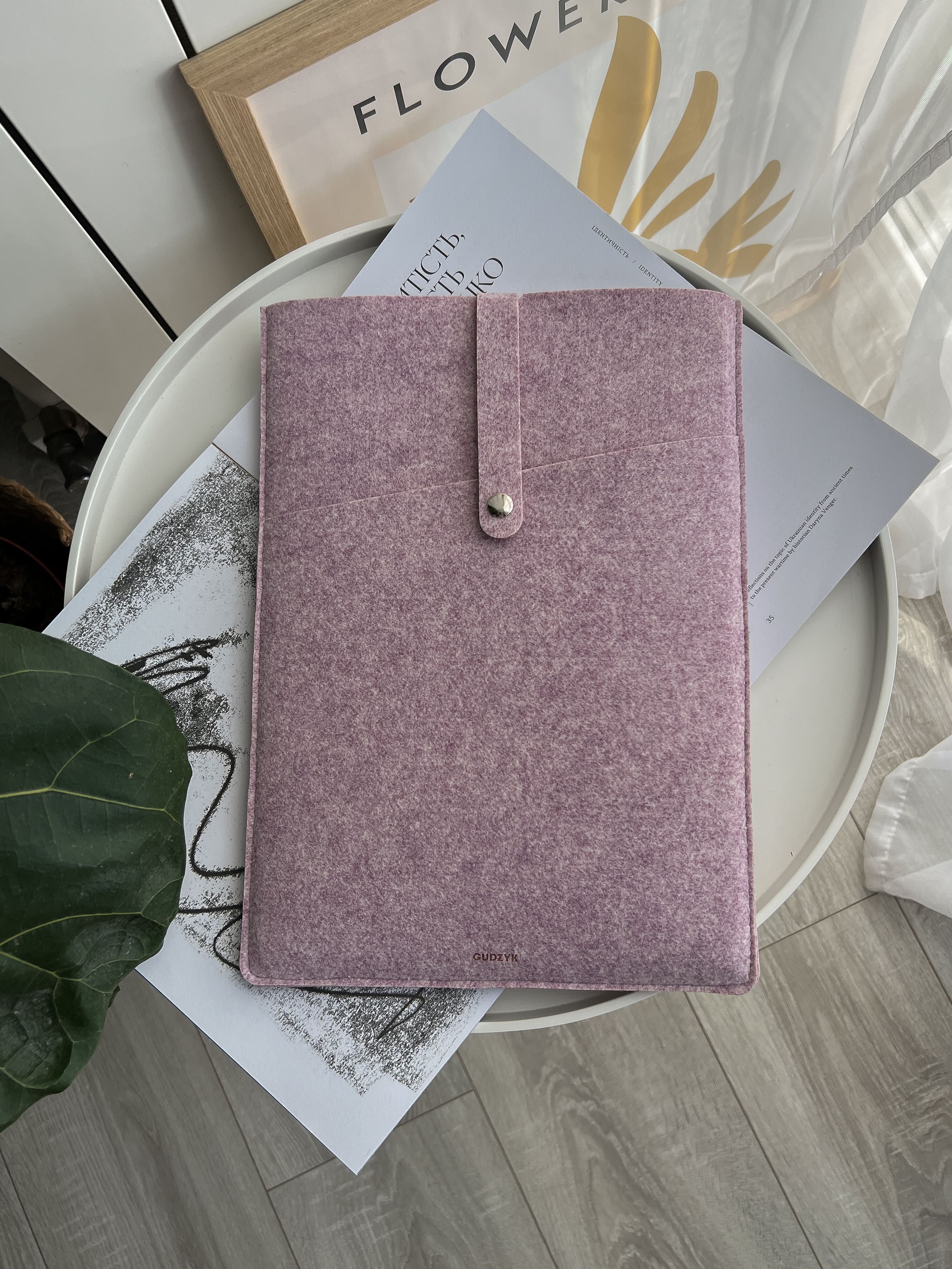 Pink laptop case on a white surface with a plant and decorative items in the background