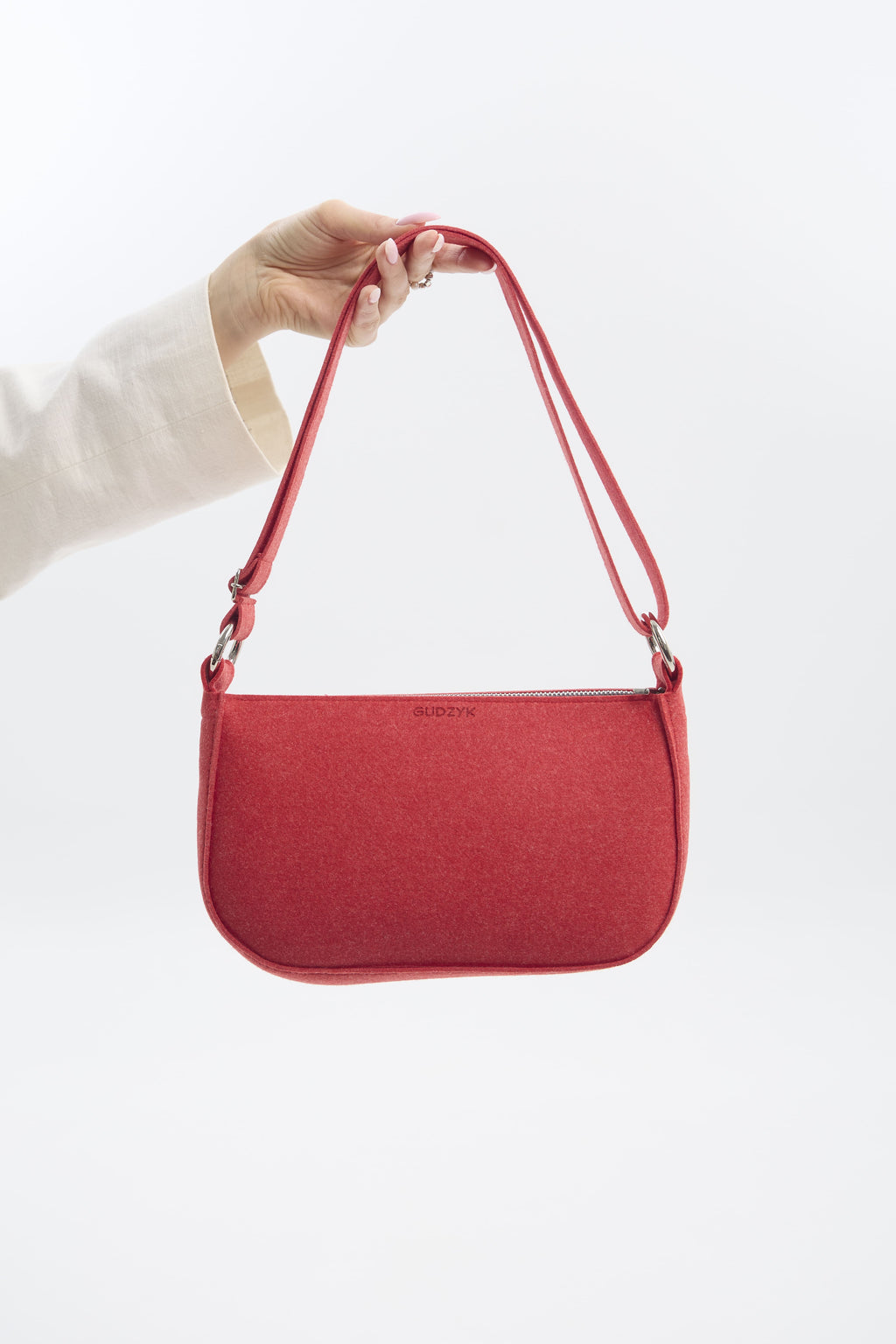 Red shoulder bag held by a hand against a white background