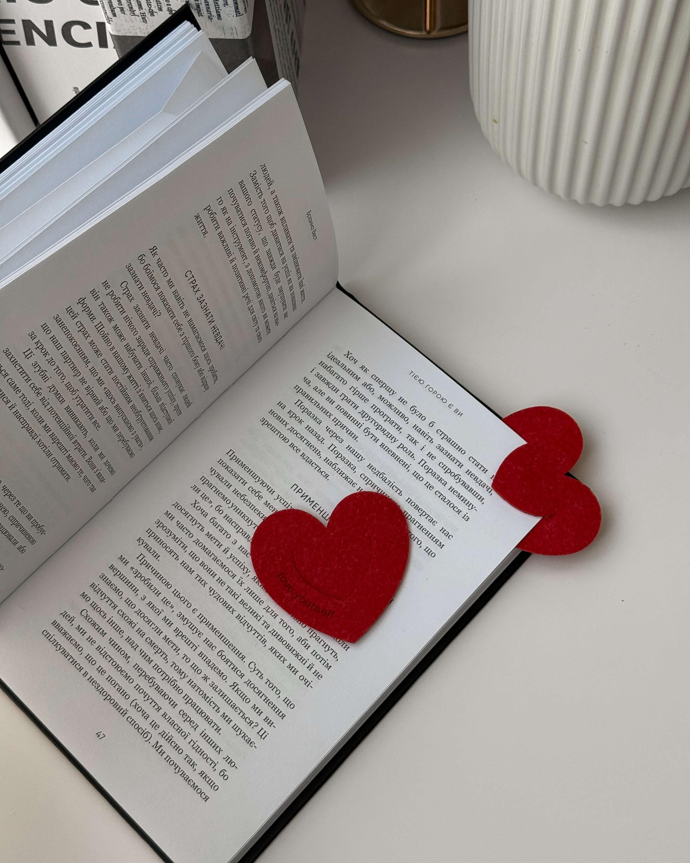 Open book with red heart-shaped bookmarks on a light surface.