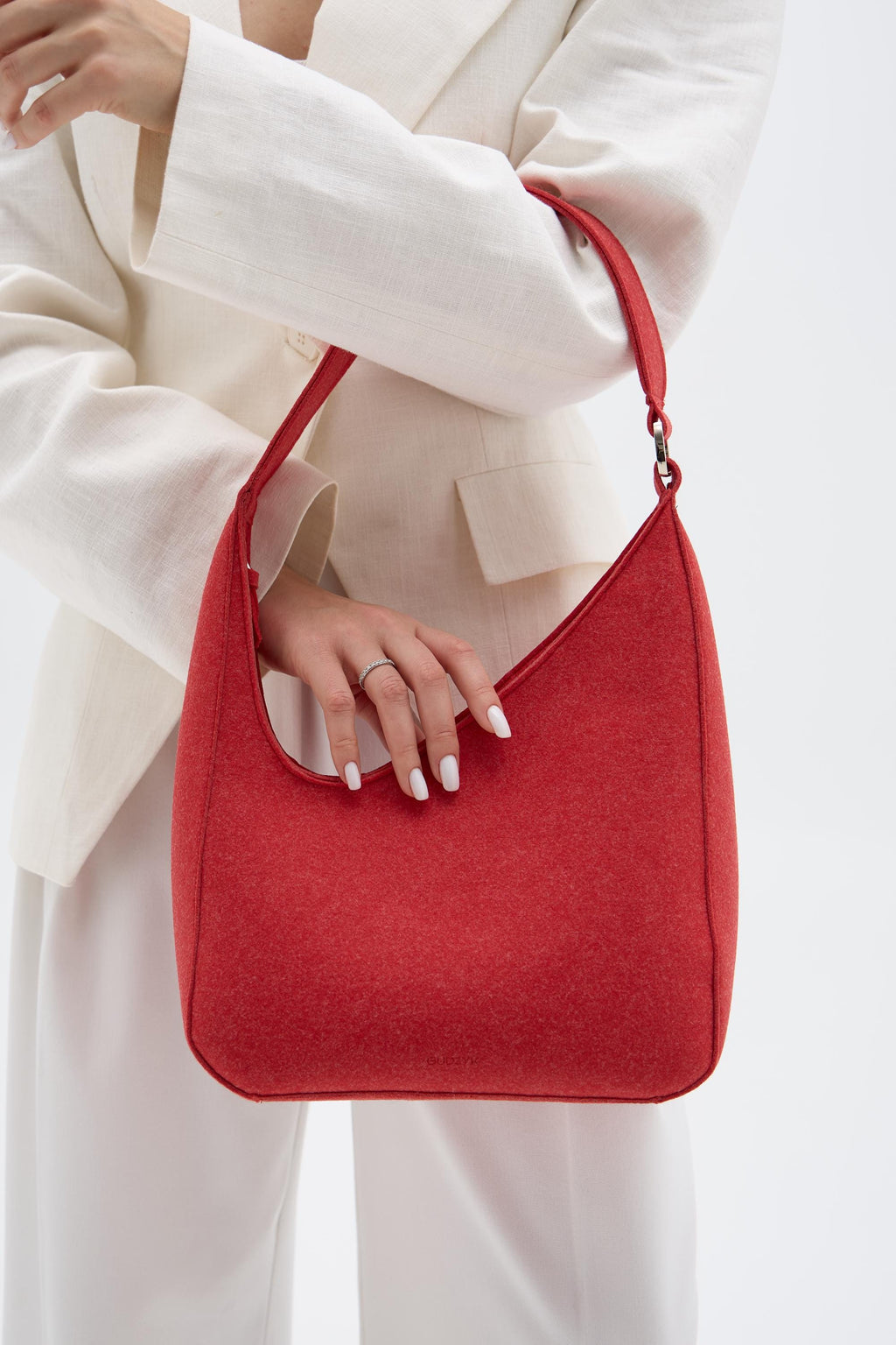 Red handbag held by a person wearing a white outfit on a light background
