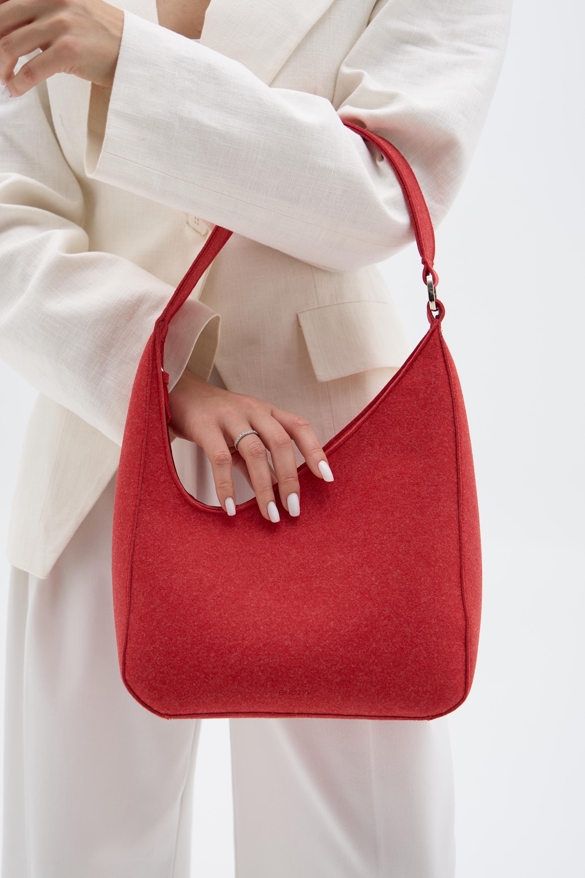 Red handbag held by a person wearing a white outfit on a light background