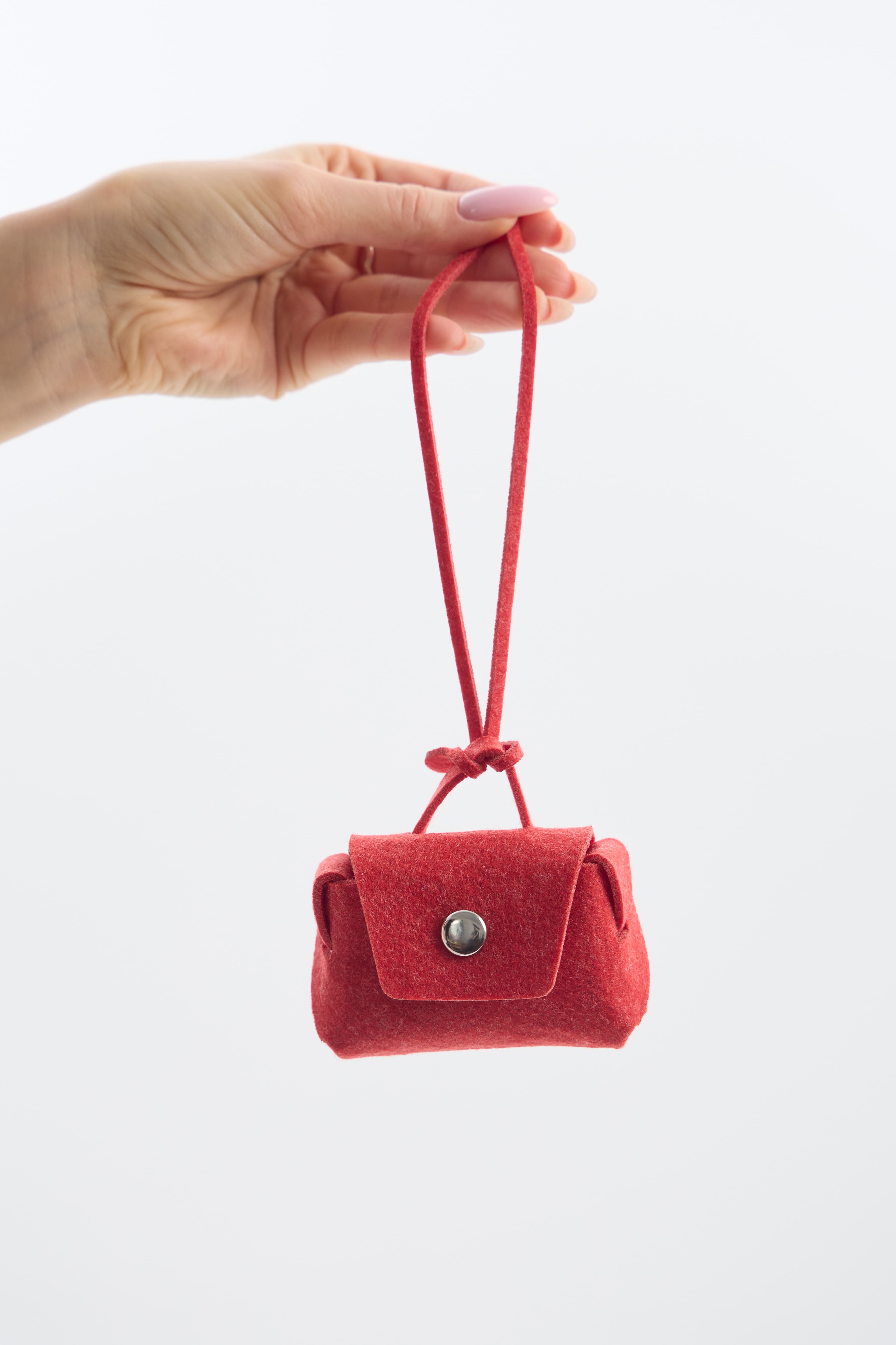 Red felt handbag held by a hand on a white background
