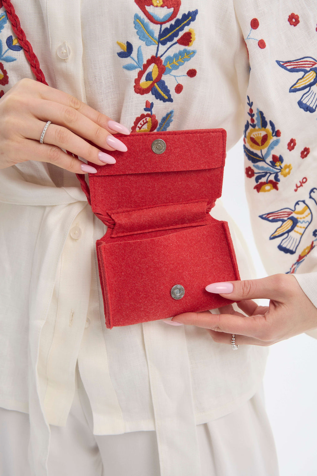 Red handbag held by a person wearing a colorful embroidered garment