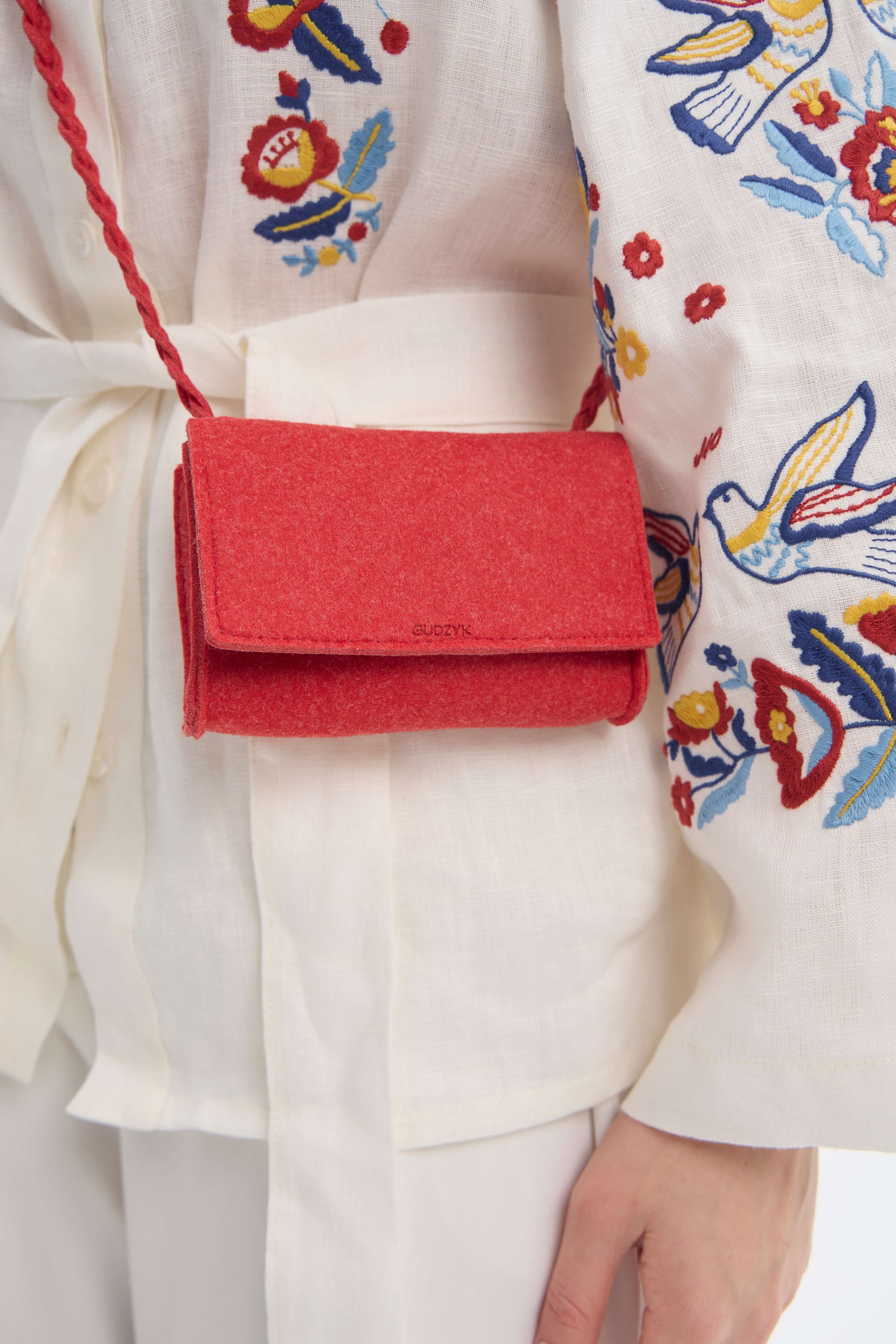 Red felt mini crossbody bag held by a person wearing a colorful embroidered garment.