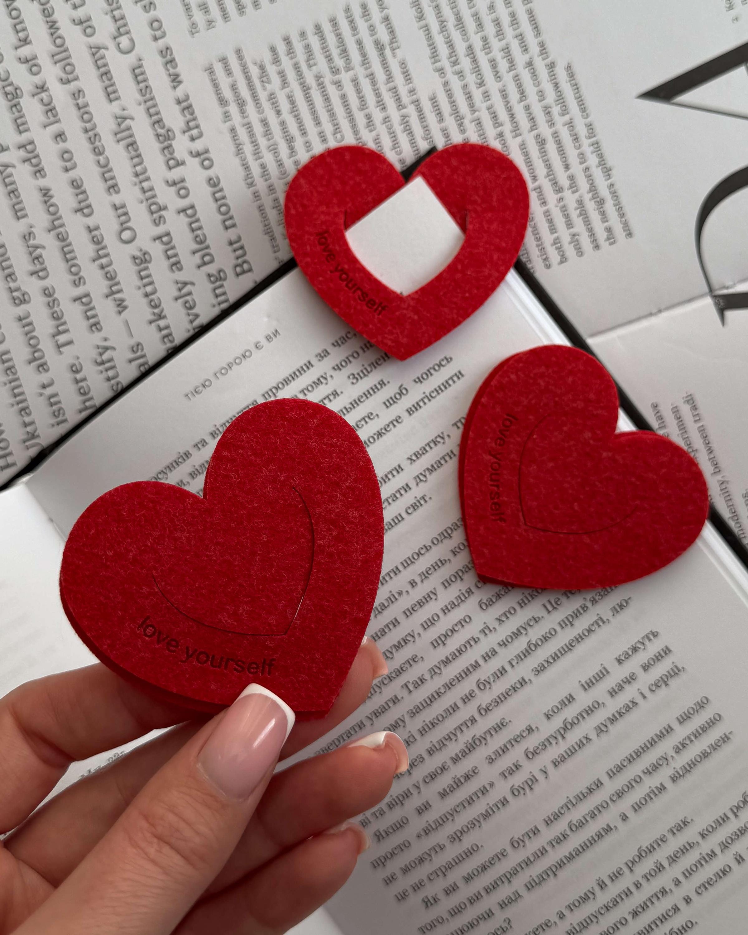 Red heart-shaped bookmark held by a hand on top of a book with text.