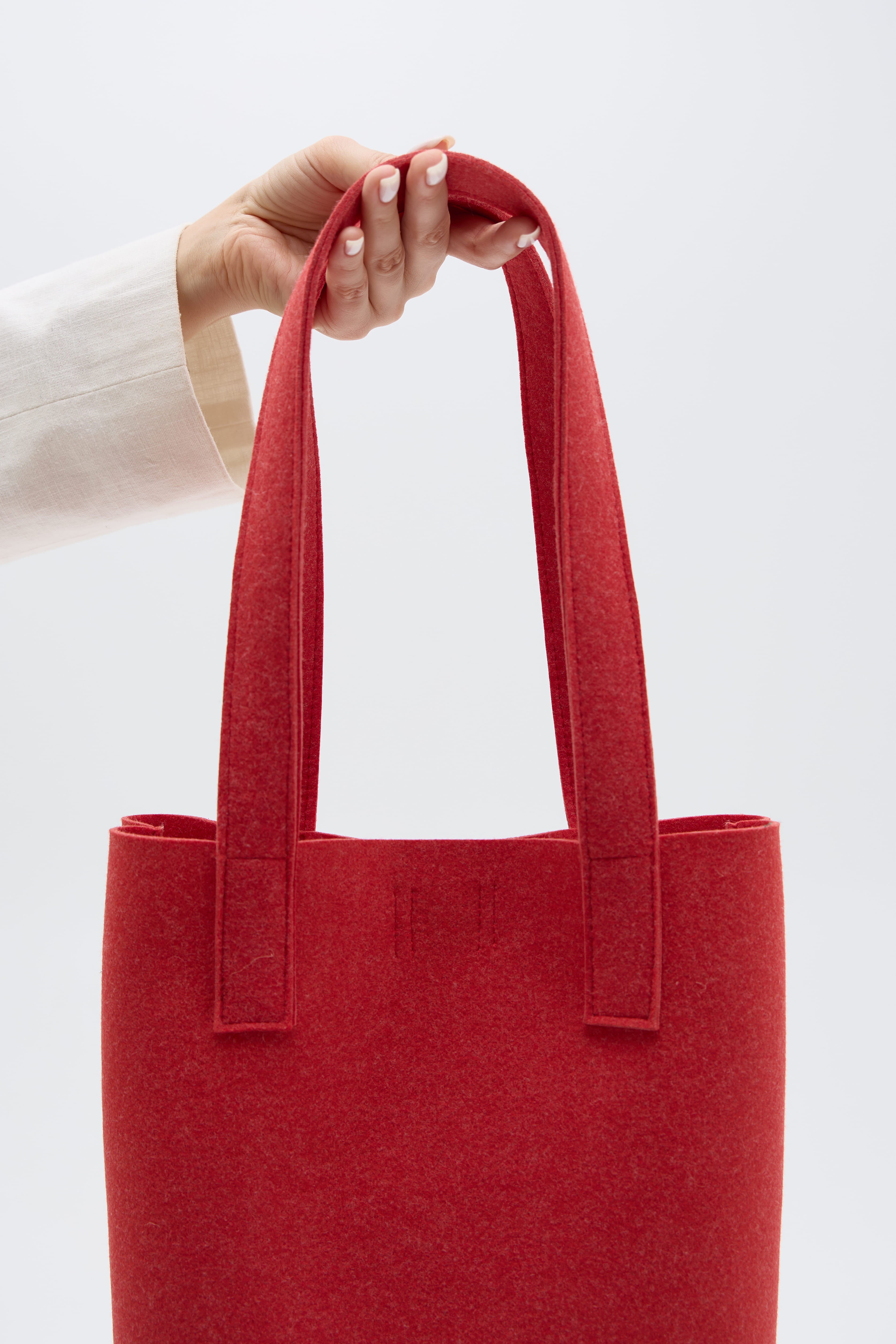 Red tote bag held by a hand against a white background