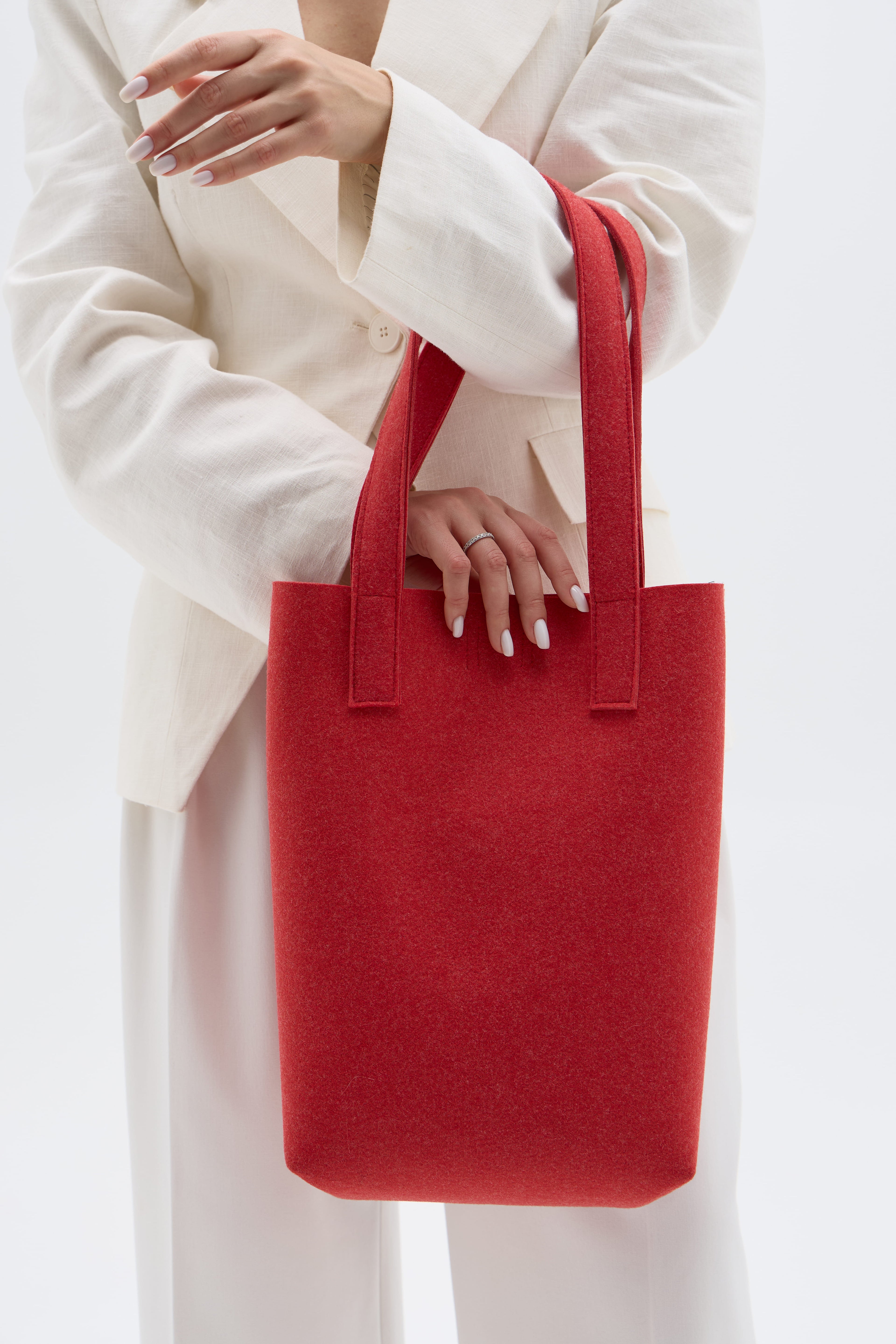 Red tote bag held by a person wearing a white outfit on a white background