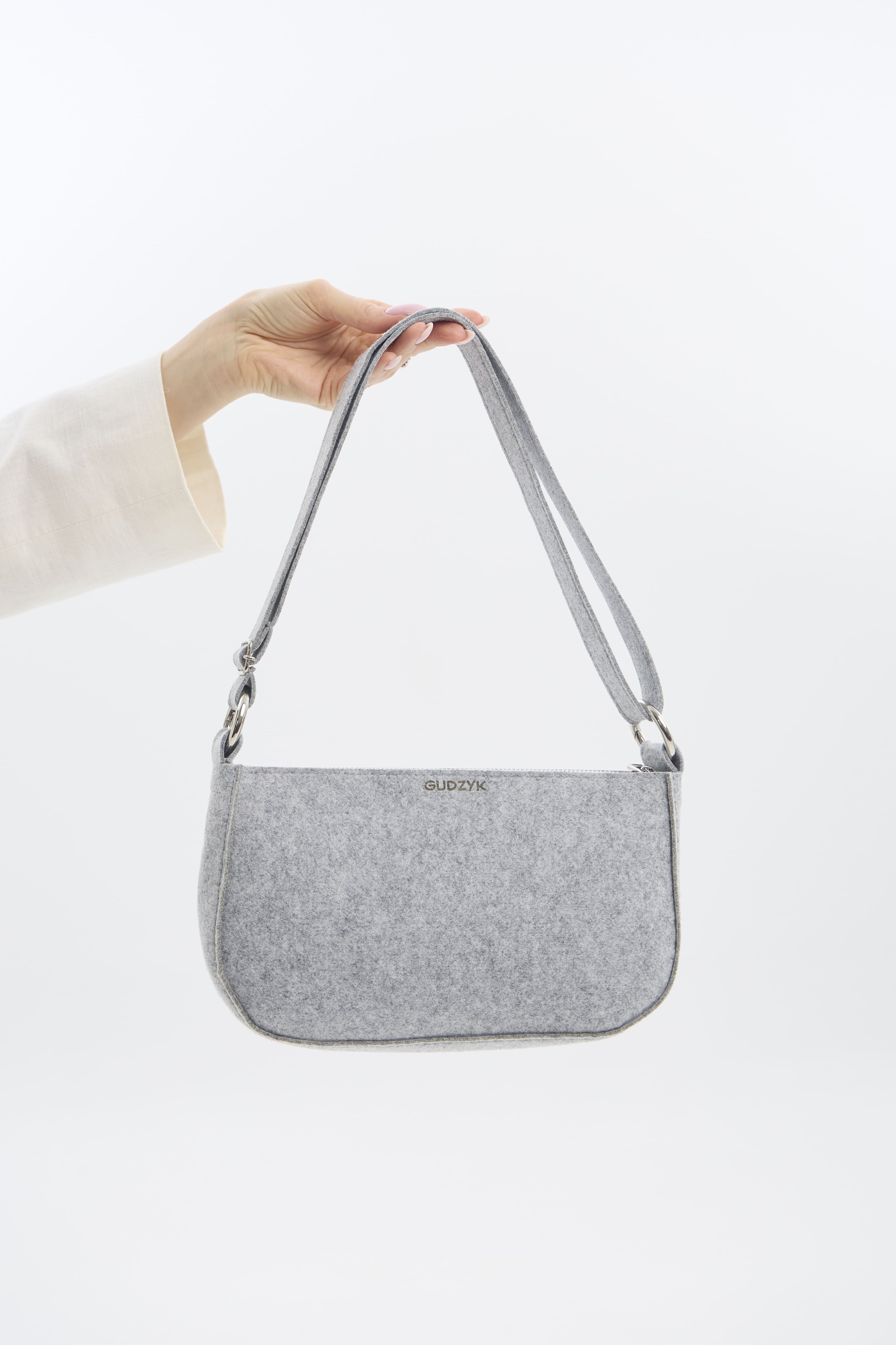 Silver shoulder bag held by a hand on a white background