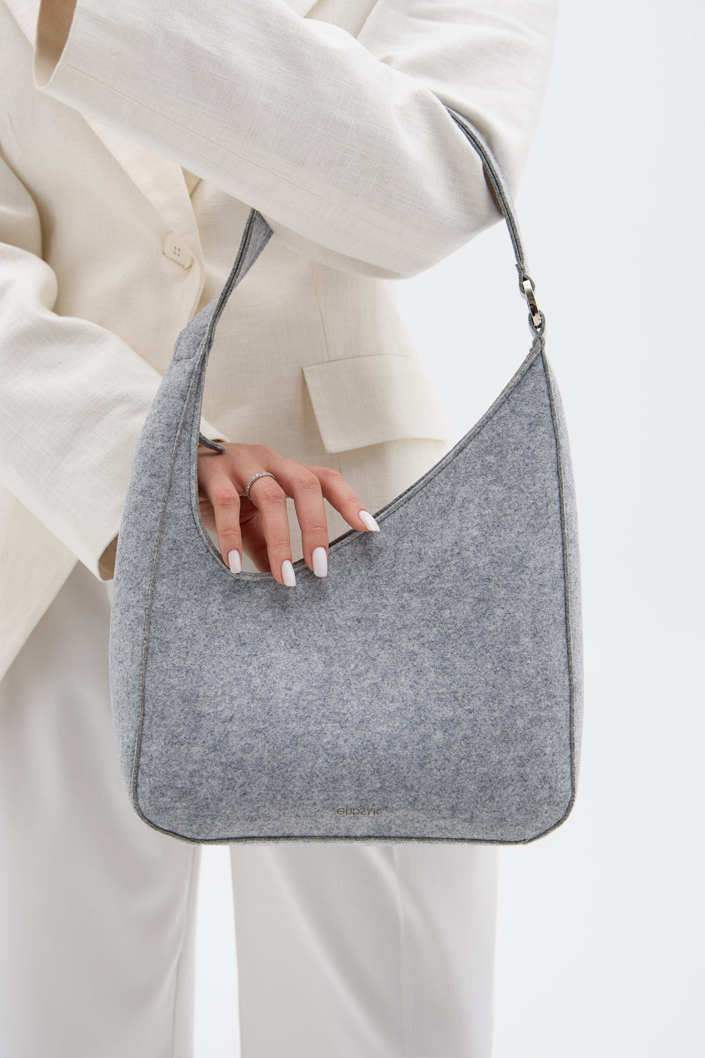 Silver handbag held by a person wearing a white outfit on a light background