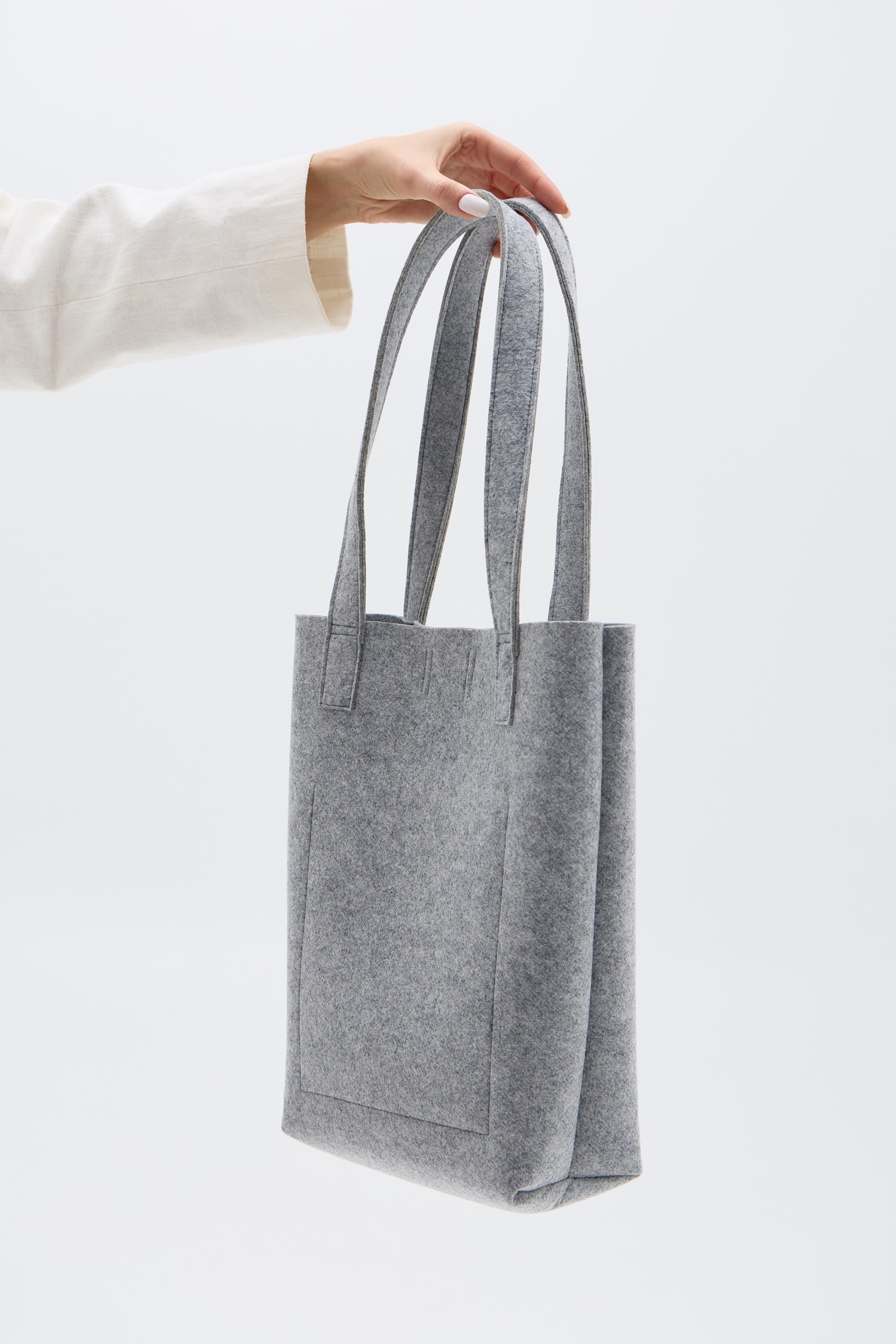 Silver tote bag held by a person against a white background