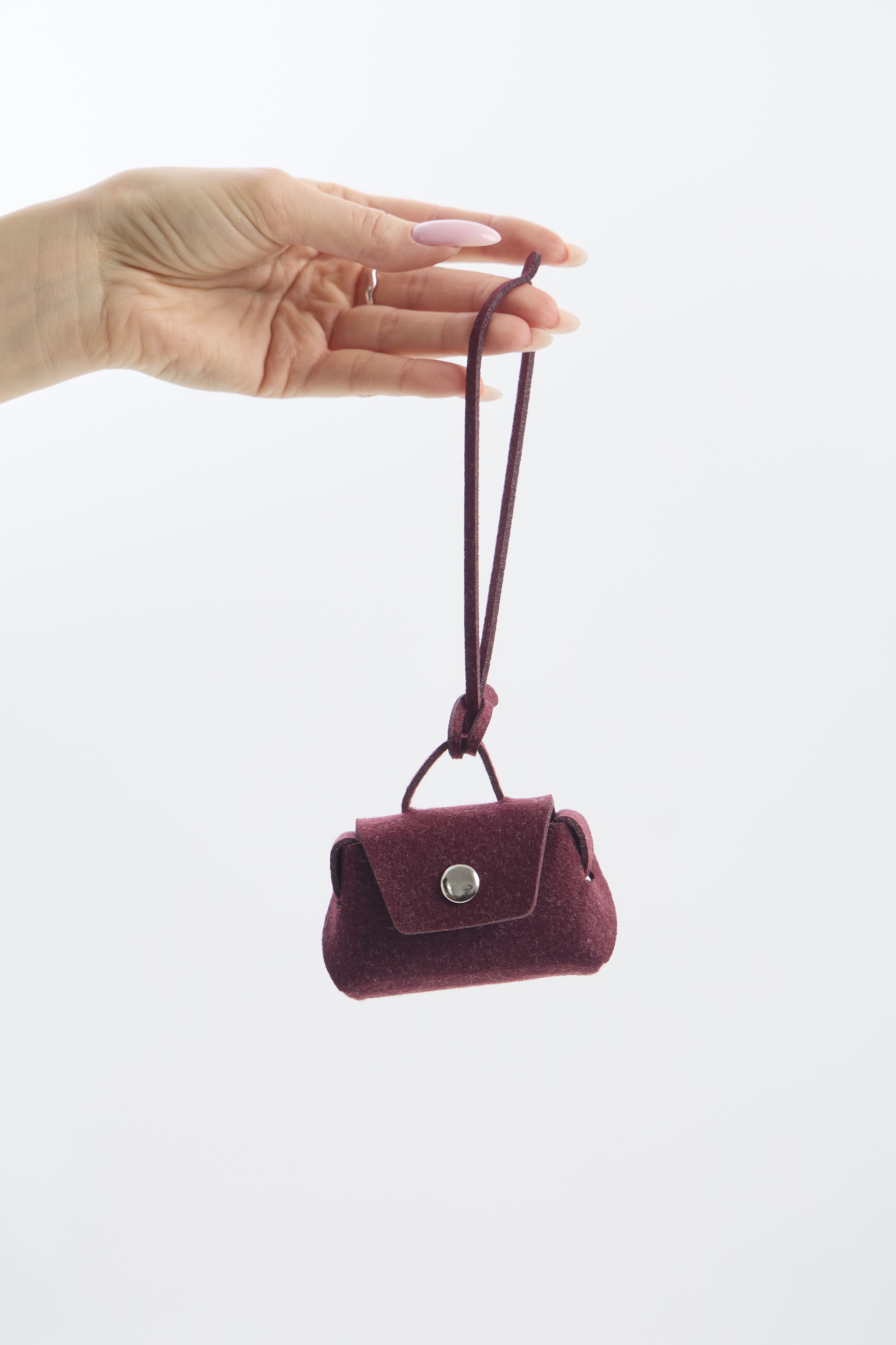 Small burgundy mini pouch with a strap held by a hand on a white background