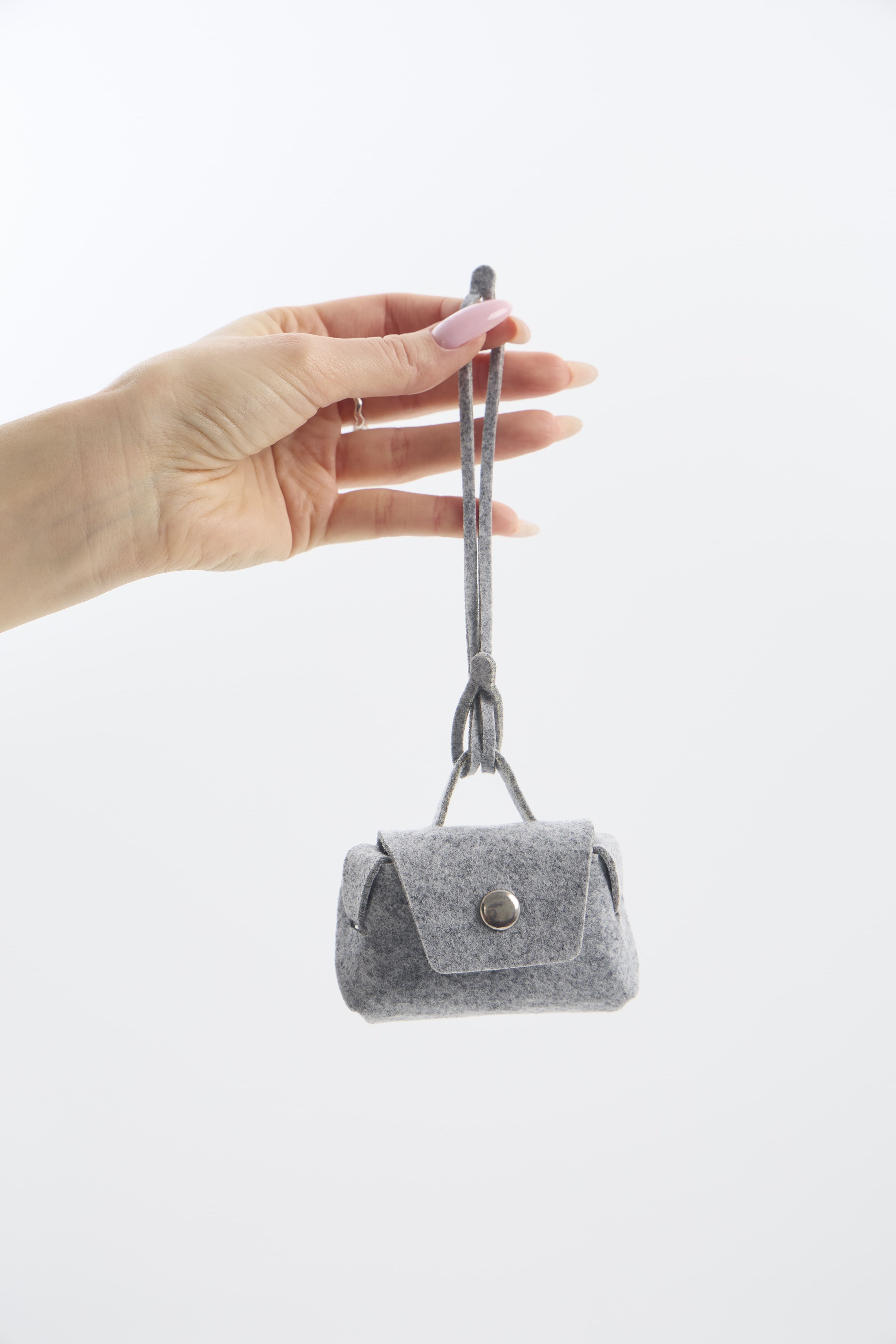 Small silver handbag with a strap held by a hand on a white background