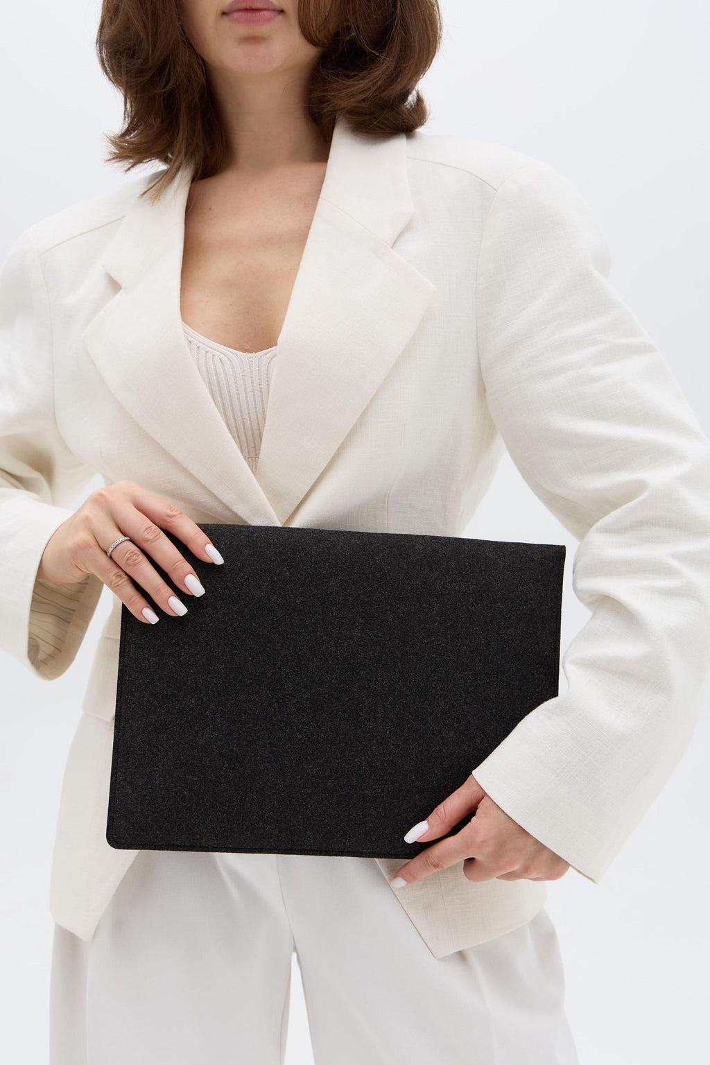 Person holding a black laptop case in a white suit against a white background
