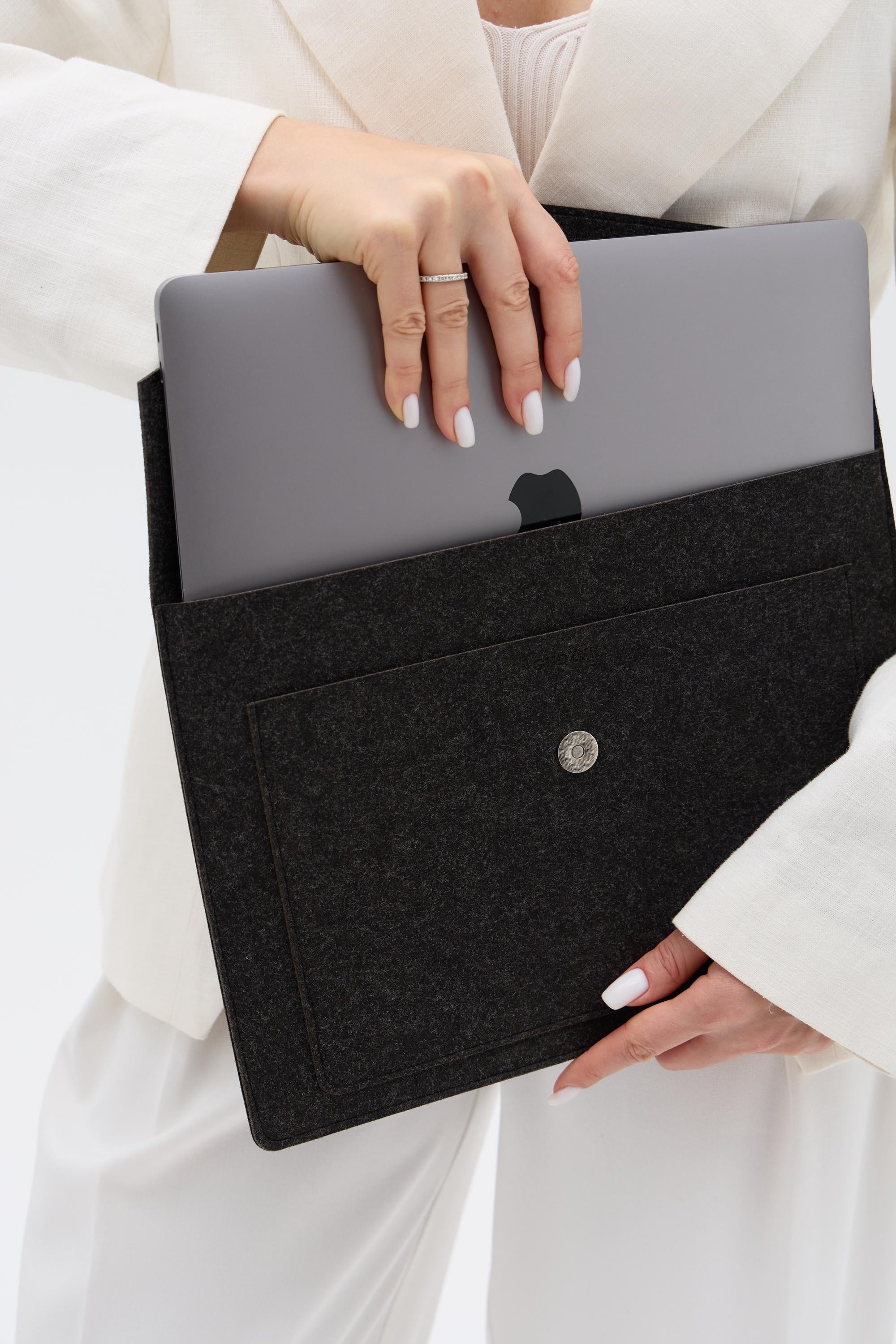 Person holding a black laptop sleeve with a gray laptop inside, wearing a white outfit.