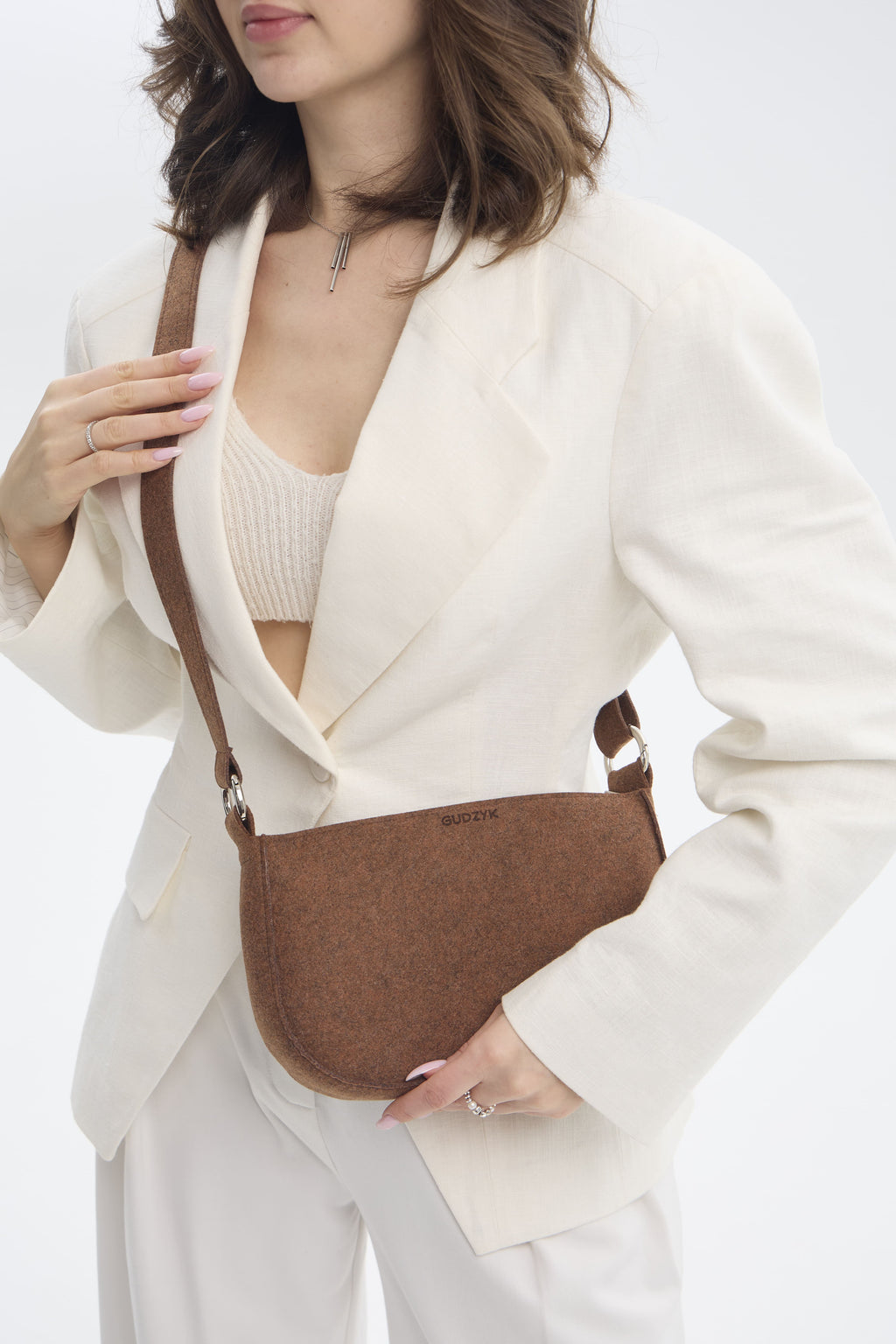 Woman wearing a white blazer and holding a brown crossbody bag on a white background