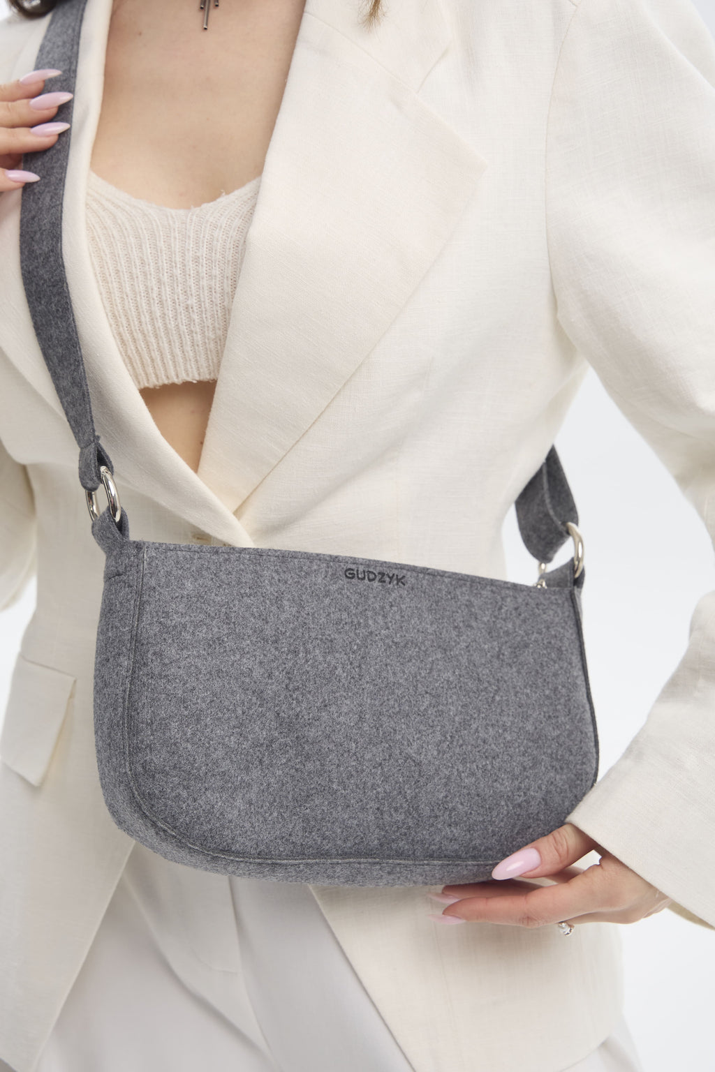 Person holding a gray crossbody bag with a visible brand logo.