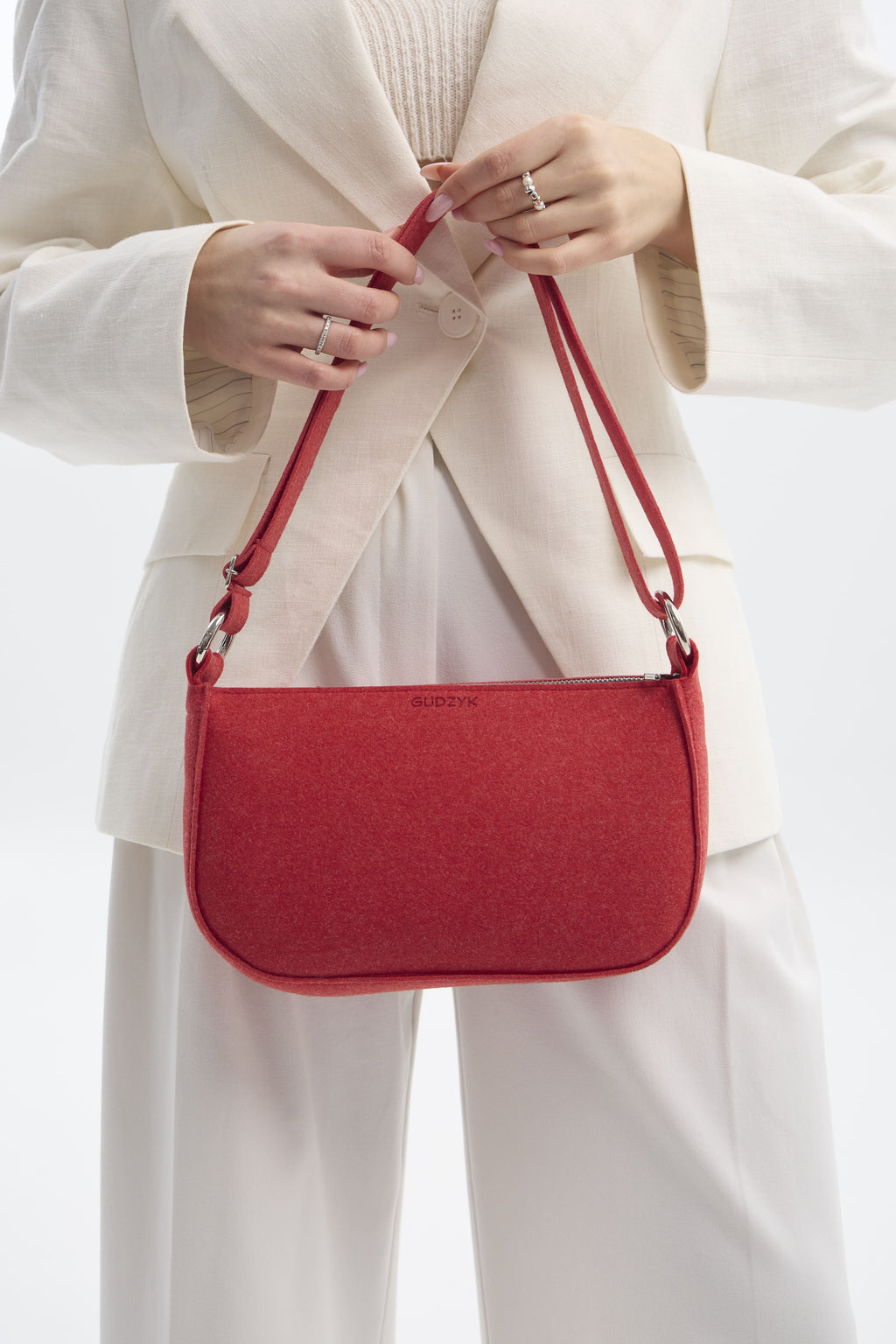 Red handbag held by a person wearing a white outfit on a white background